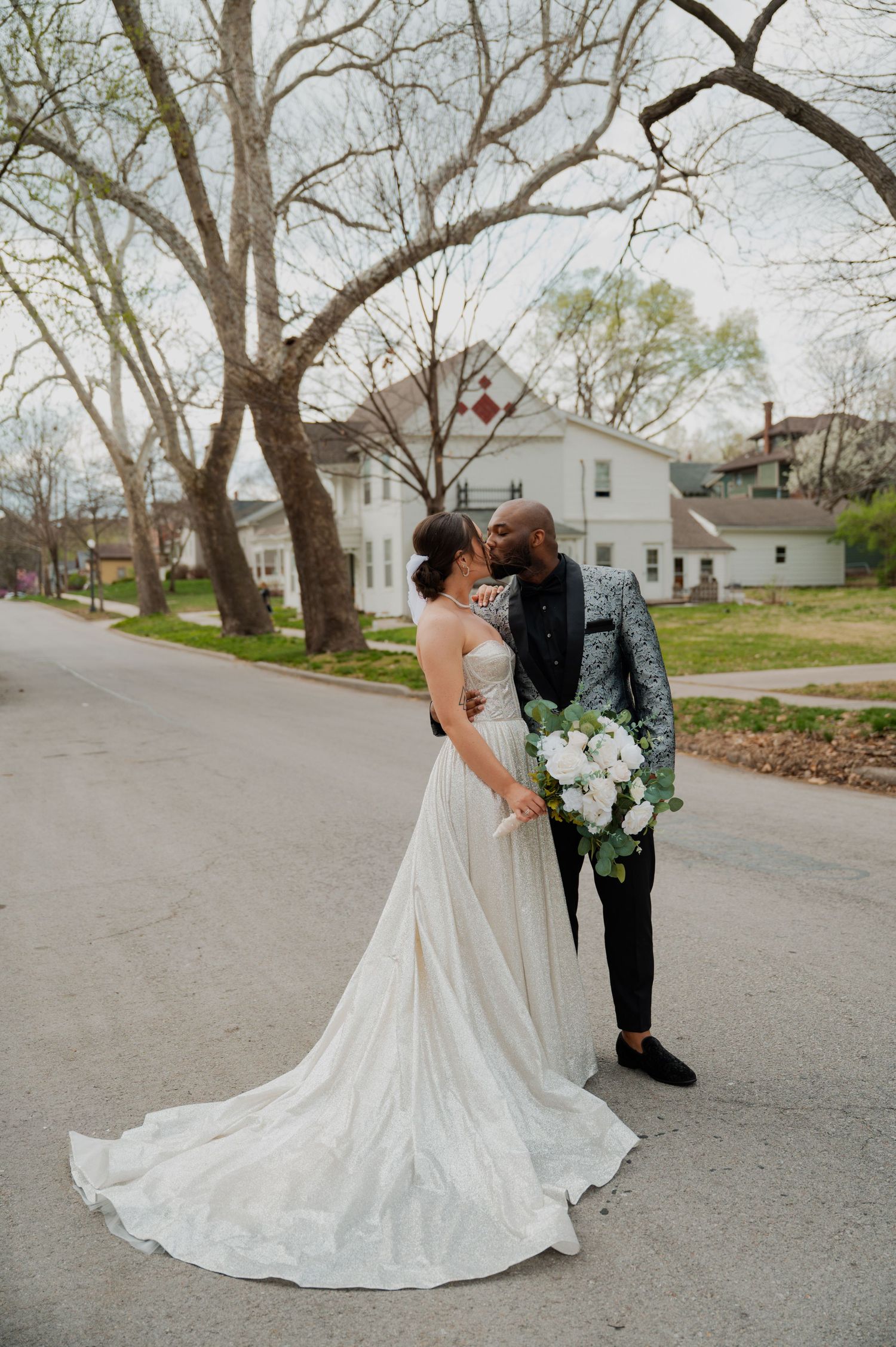 A romantic wedding couple shares an intimate moment on a tree-lined street in spring.
