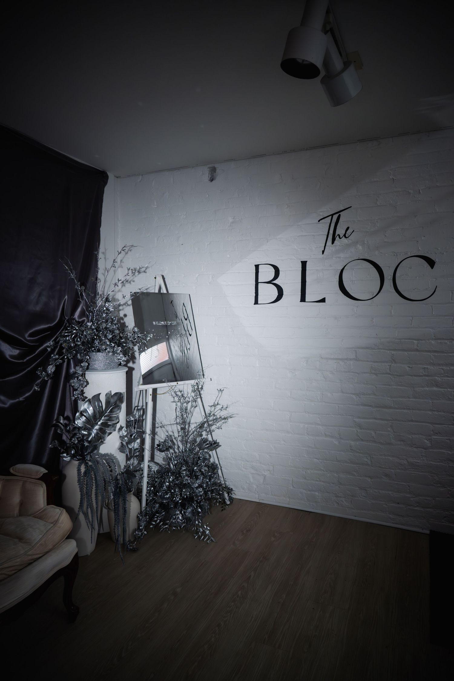 Moody interior of The Bloc venue featuring white brick wall signage, decorative plants, and elegant dark drapery.
