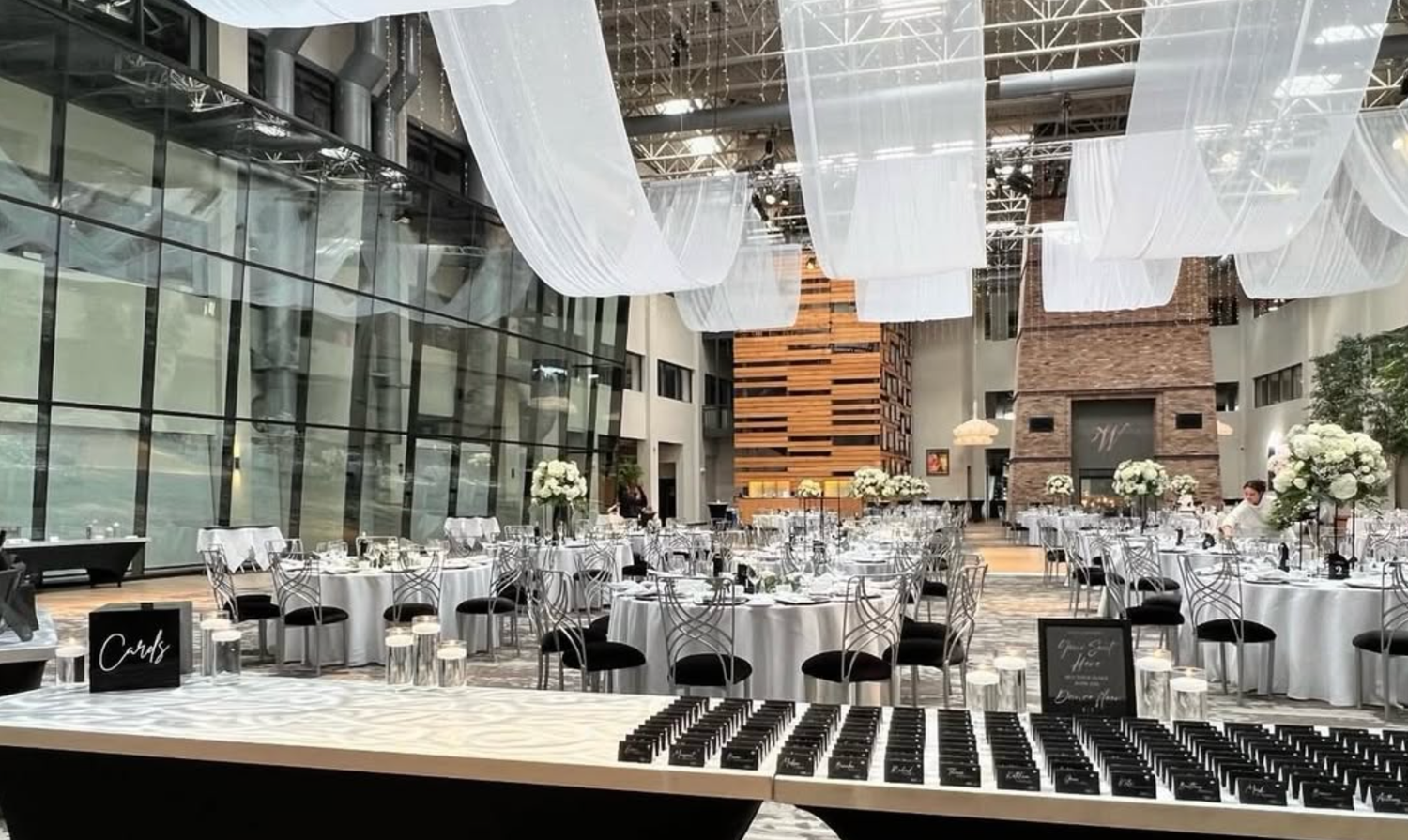 Modern wedding ceremony venue with white chairs and floral arrangements in an industrial-style space with high ceilings.