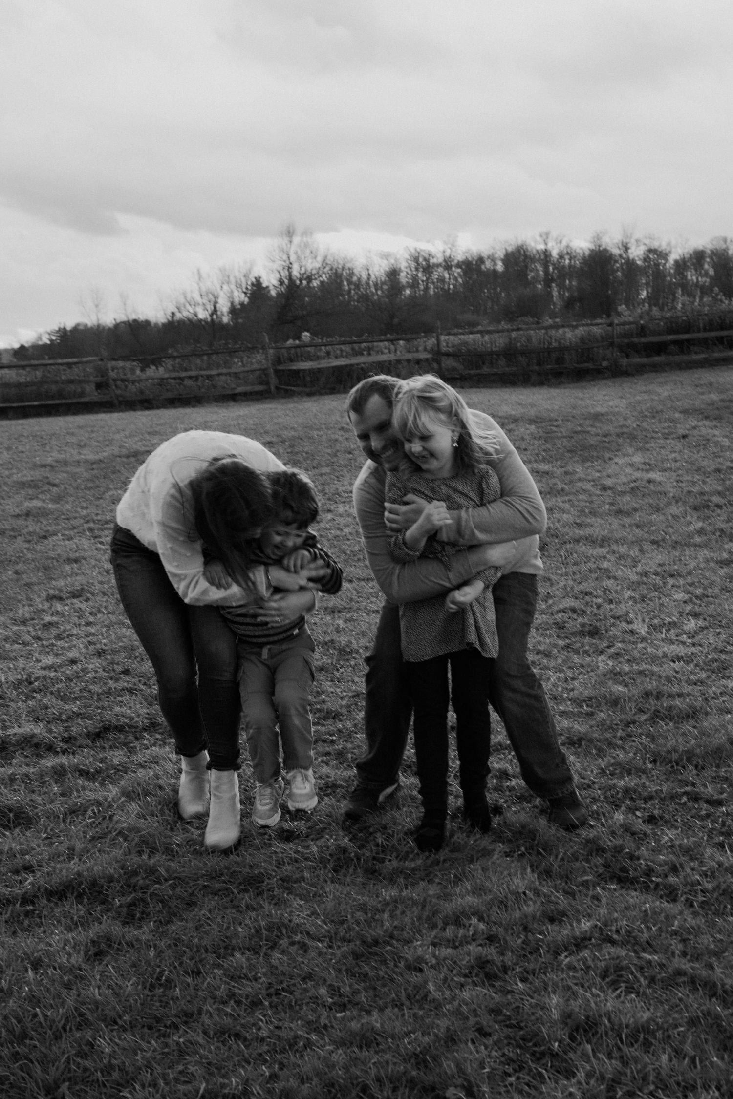 Black and white family photo of parents hugging children in a grassy field with trees in the background.