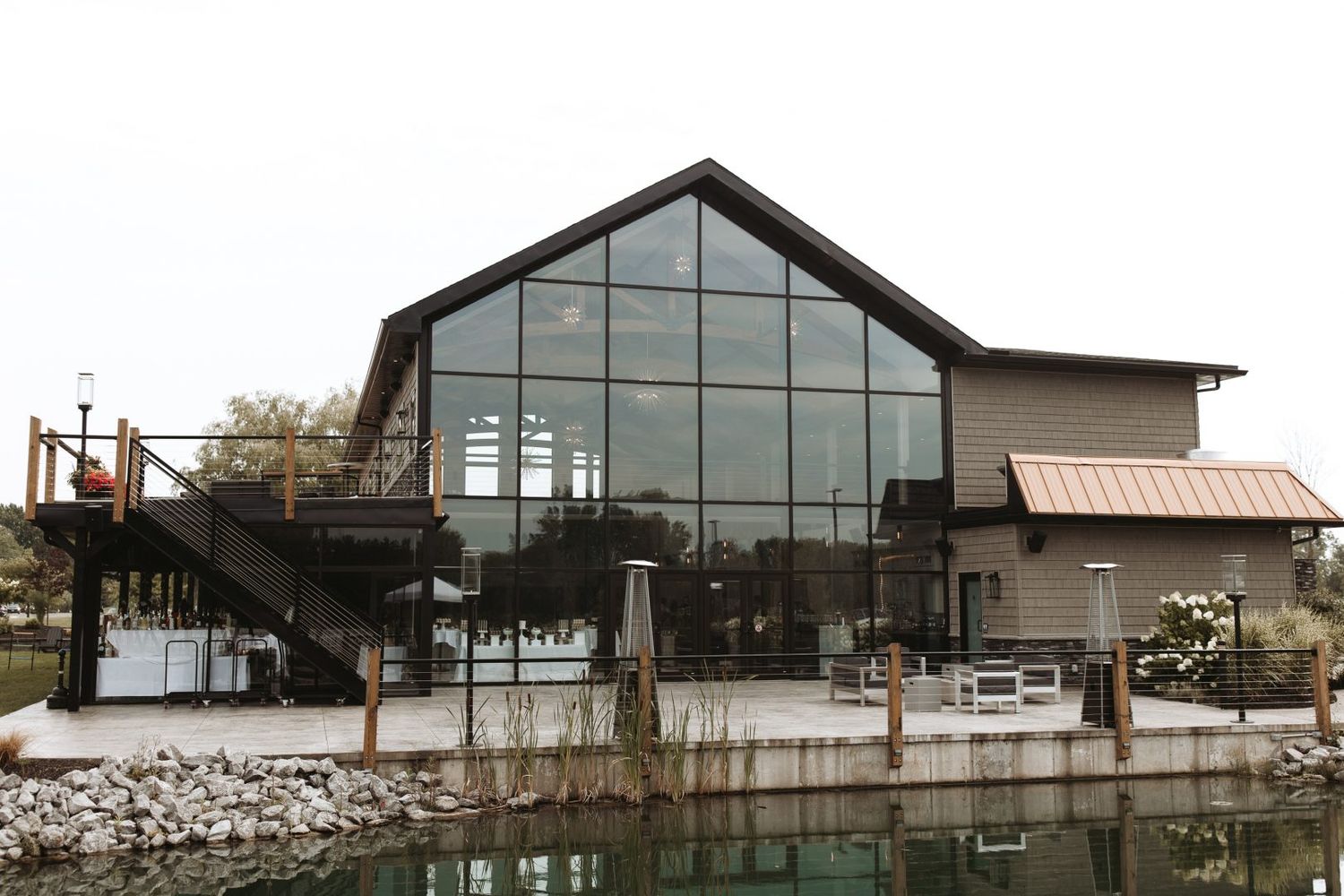 Modern waterfront building with large glass windows and rustic wood exterior sits along a tranquil pond.