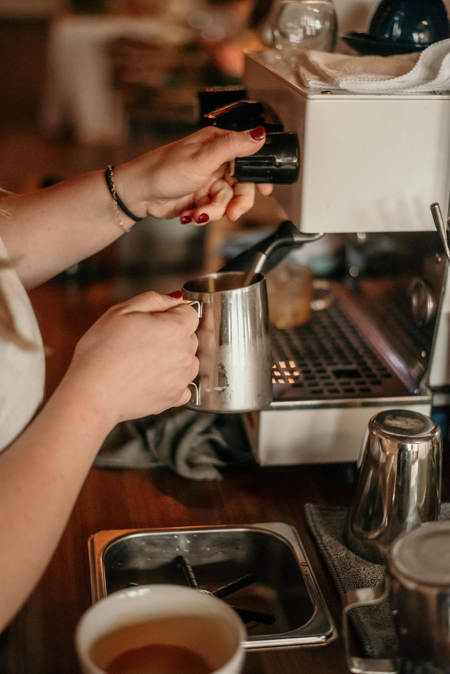 Barista steaming milk in a silver pitcher using a professional espresso machine in a cozy café setting.