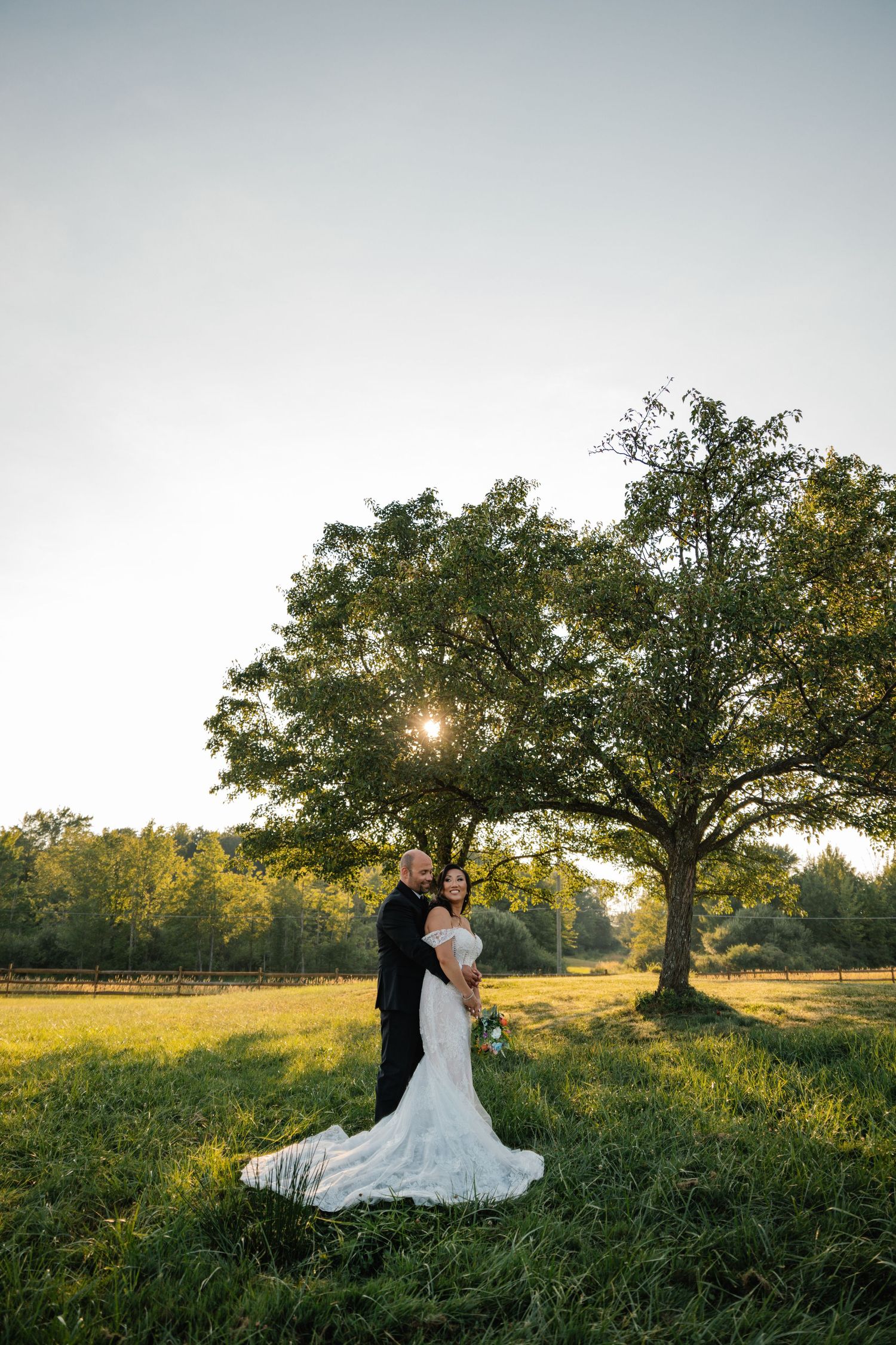 A couple embraces in a romantic sunset photoshoot under a majestic oak tree in a golden meadow.