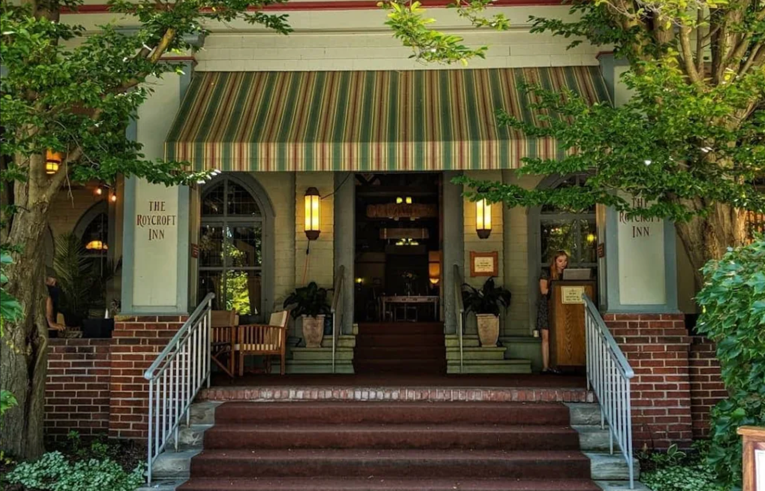 A charming brick building entrance with striped awnings, potted plants, and steps leading to a welcoming front door.