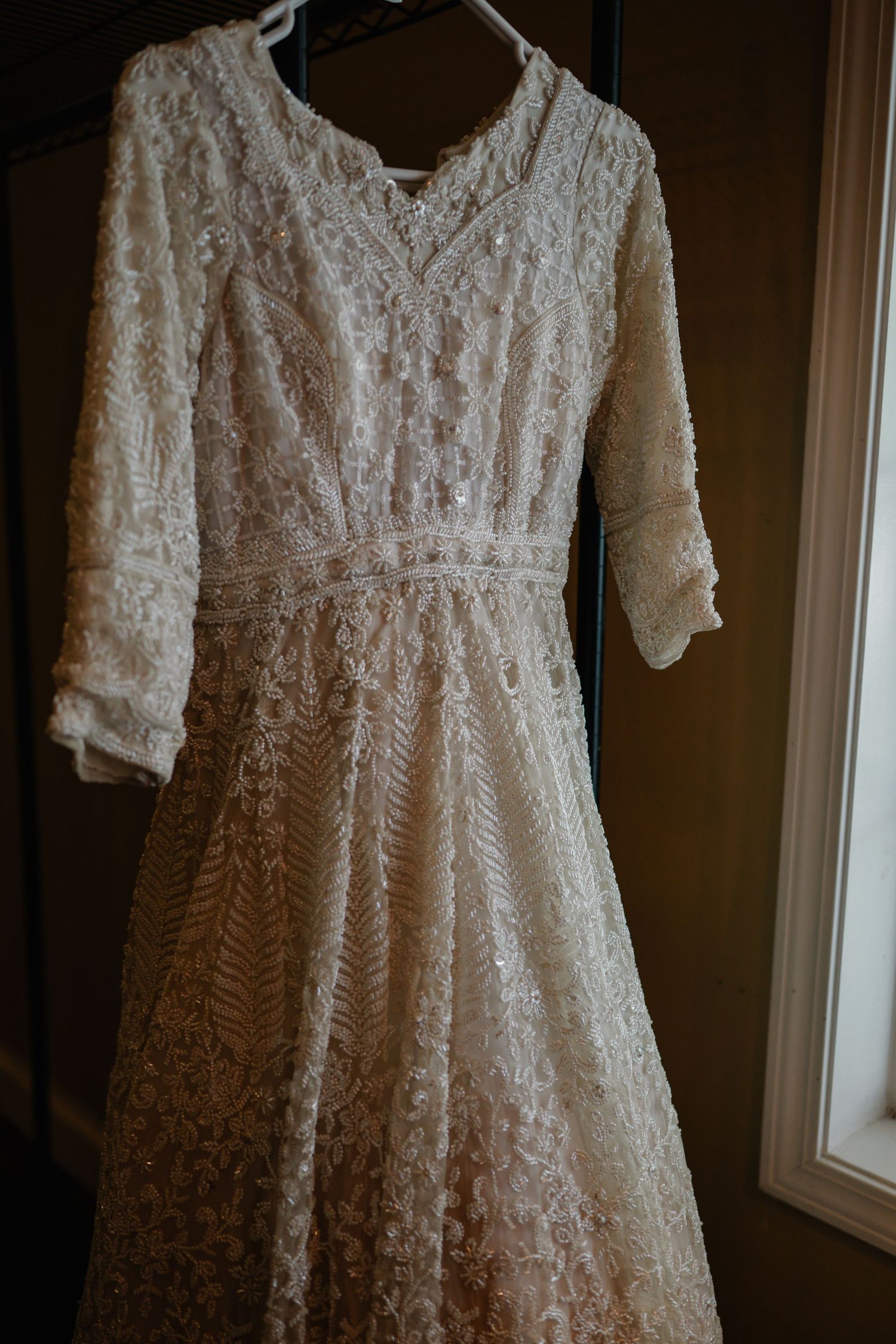 Elegant ivory lace wedding dress with 3/4 sleeves and empire waist hanging on a hanger.