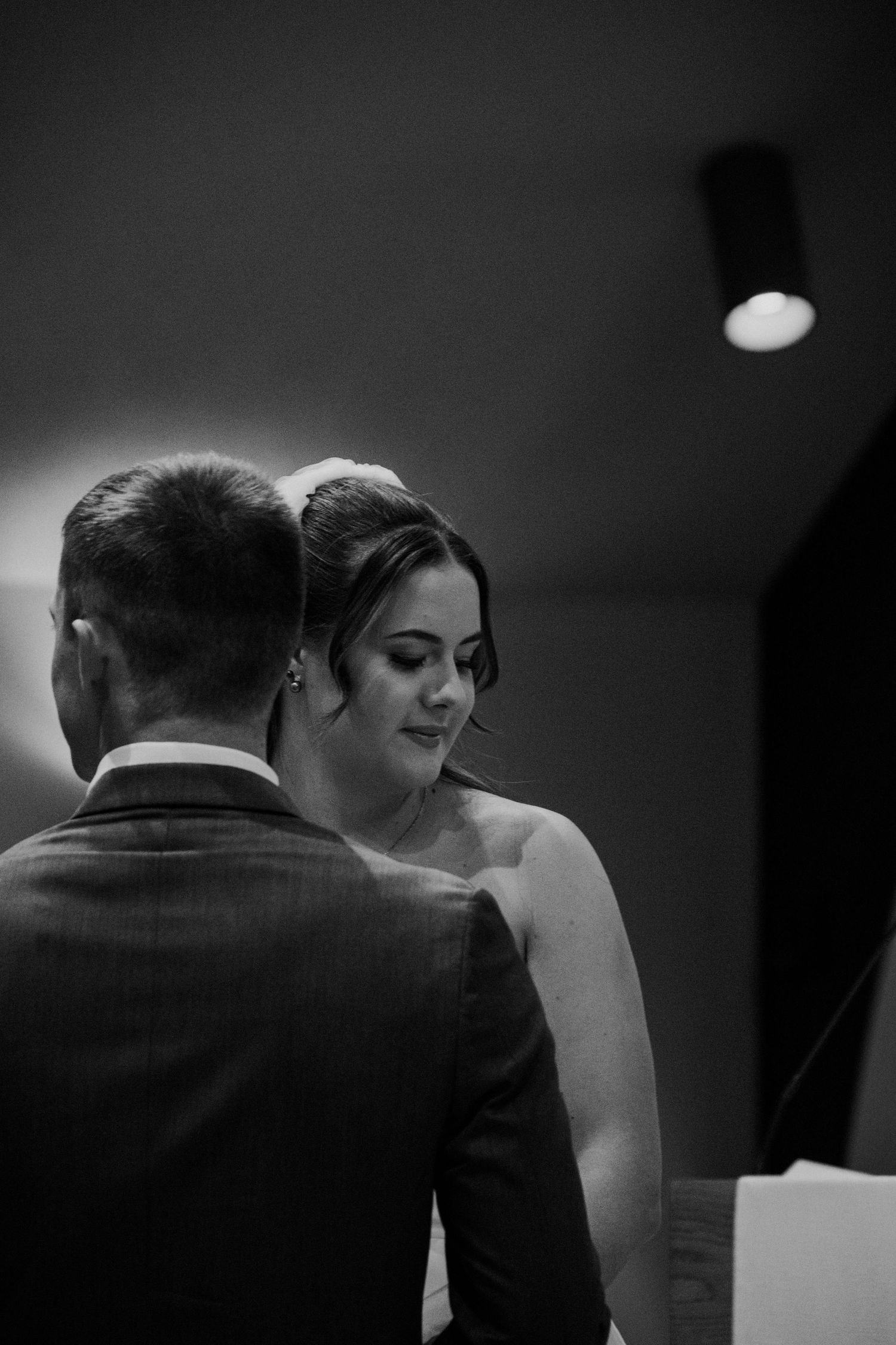 Black and white photo of a bride and groom sharing an intimate moment during their wedding ceremony indoors.