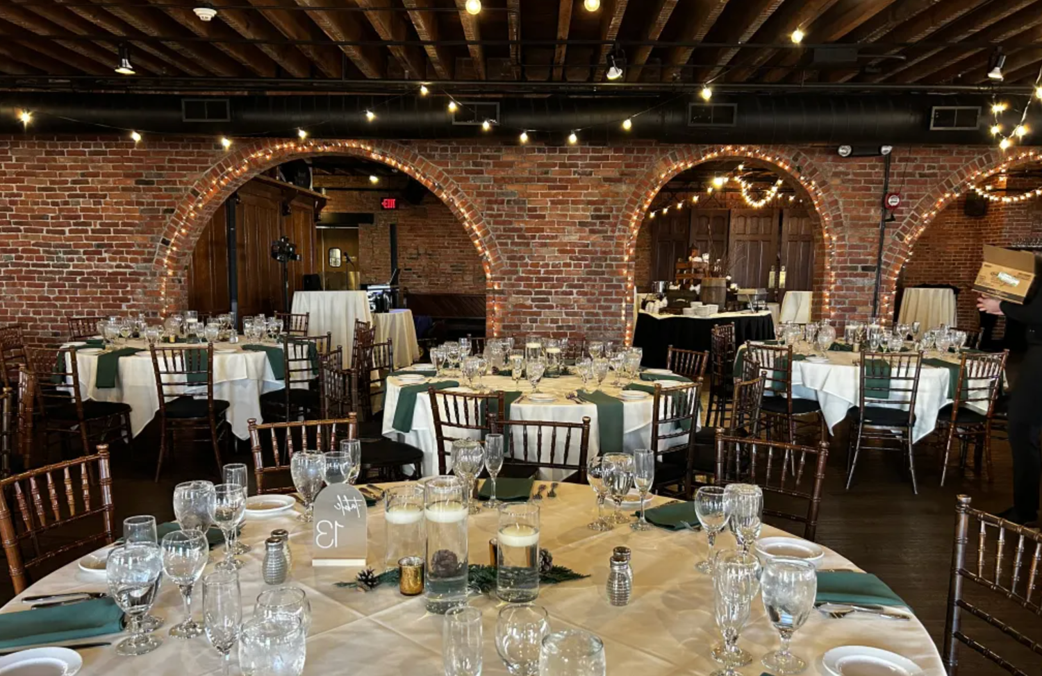 A panoramic view of a rustic brick-walled event venue with elegant table settings and string lights overhead.