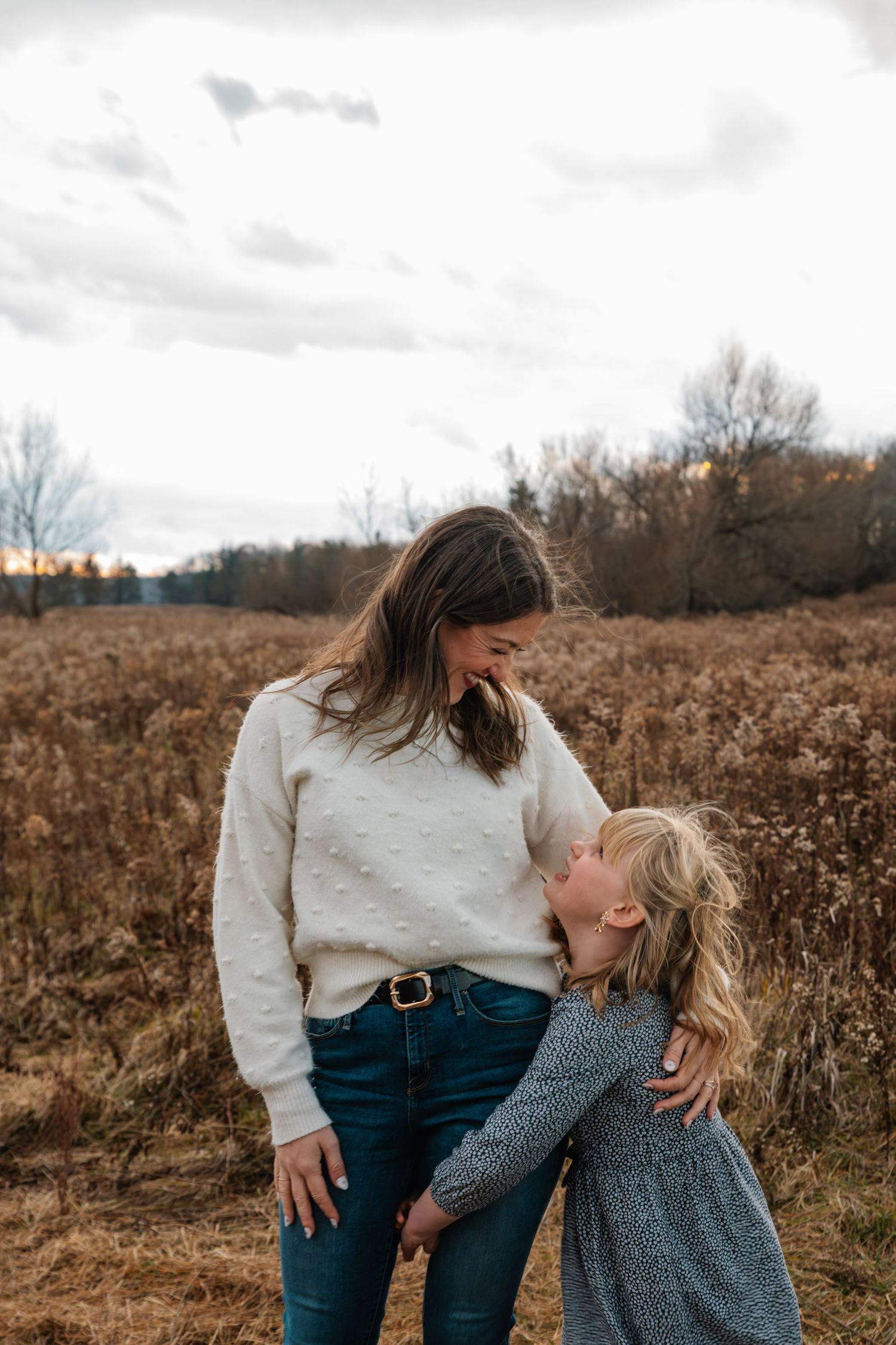 A mother and young daughter share a tender moment in an autumn field, the girl leaning in for a kiss.