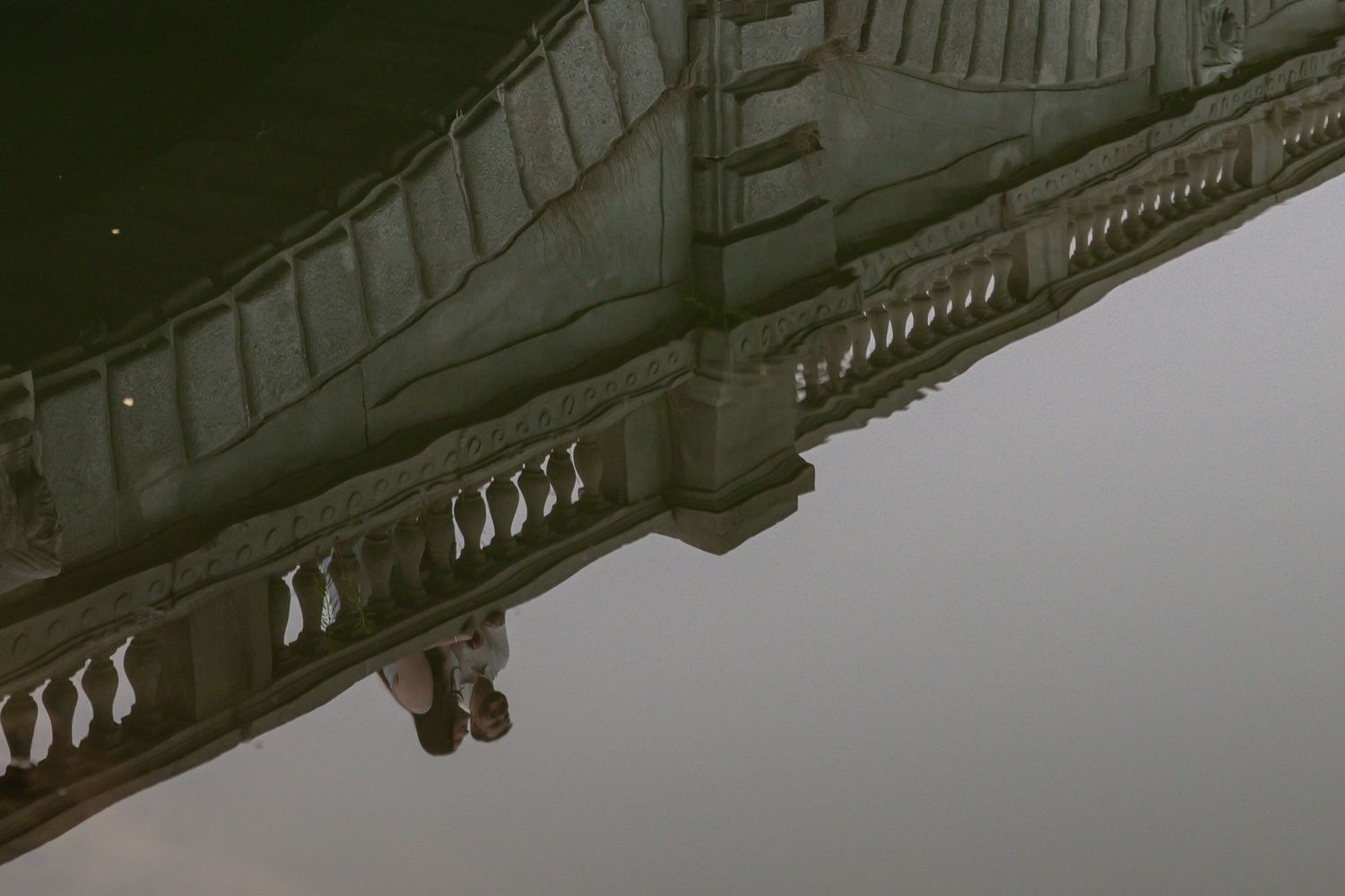 Reflection of ornate building with balustrade and arches mirrored in still water, creating surreal upside-down architectural image.