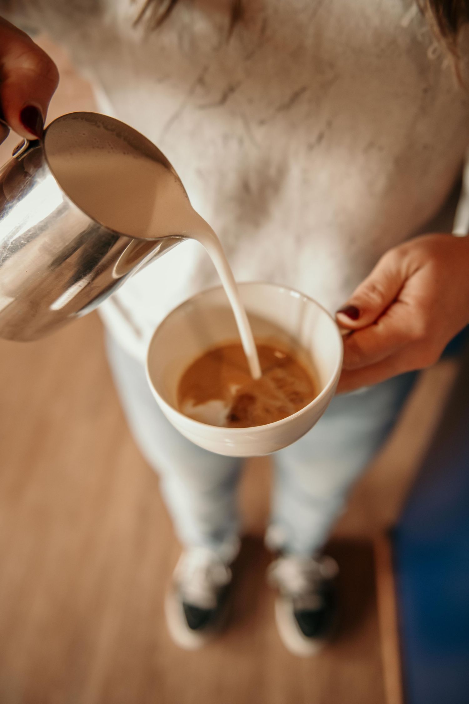 Barista pouring steamed milk from a steel pitcher into a coffee cup, creating latte art.