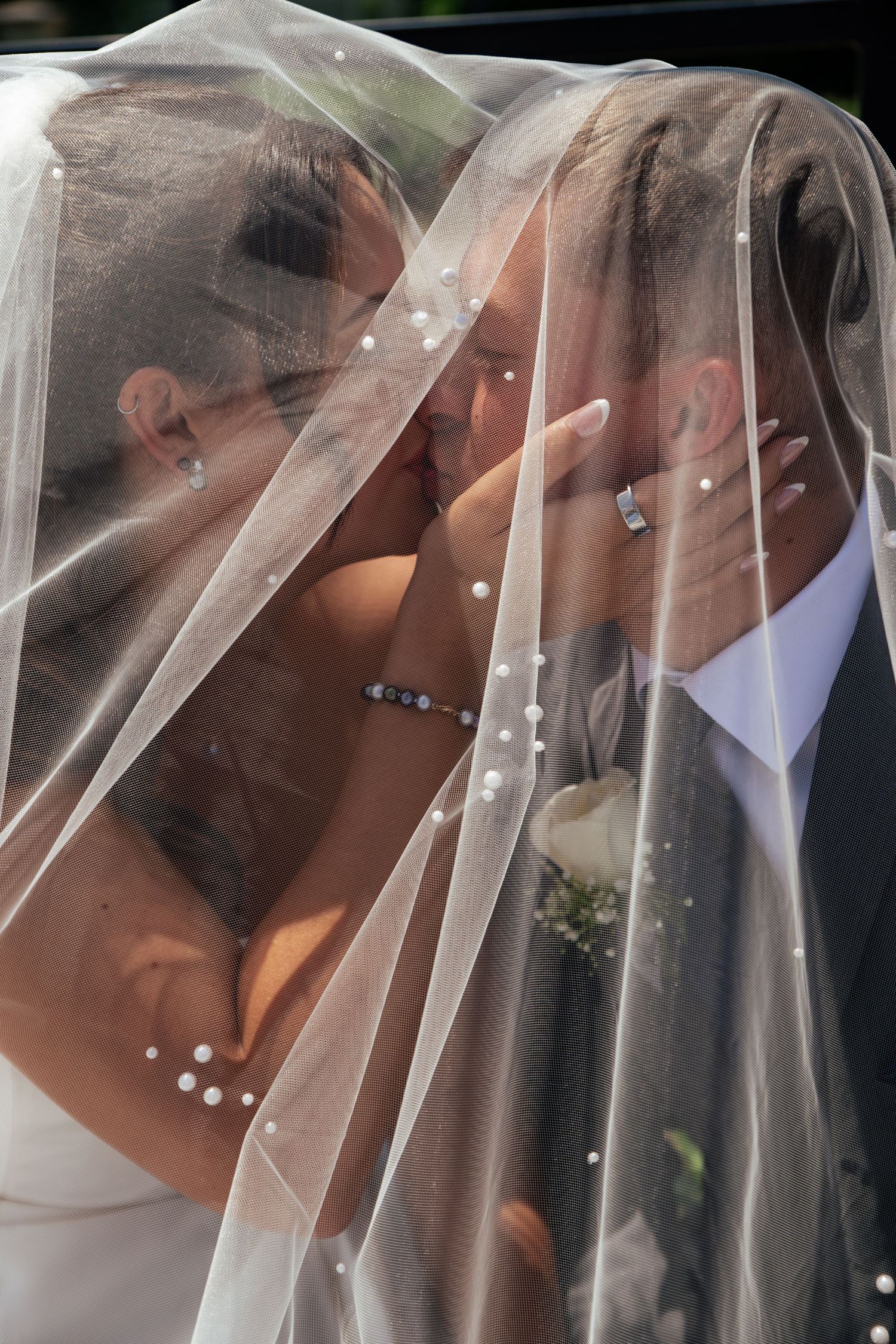 Bride and groom sharing a romantic kiss under a pearl-adorned wedding veil on their special day.