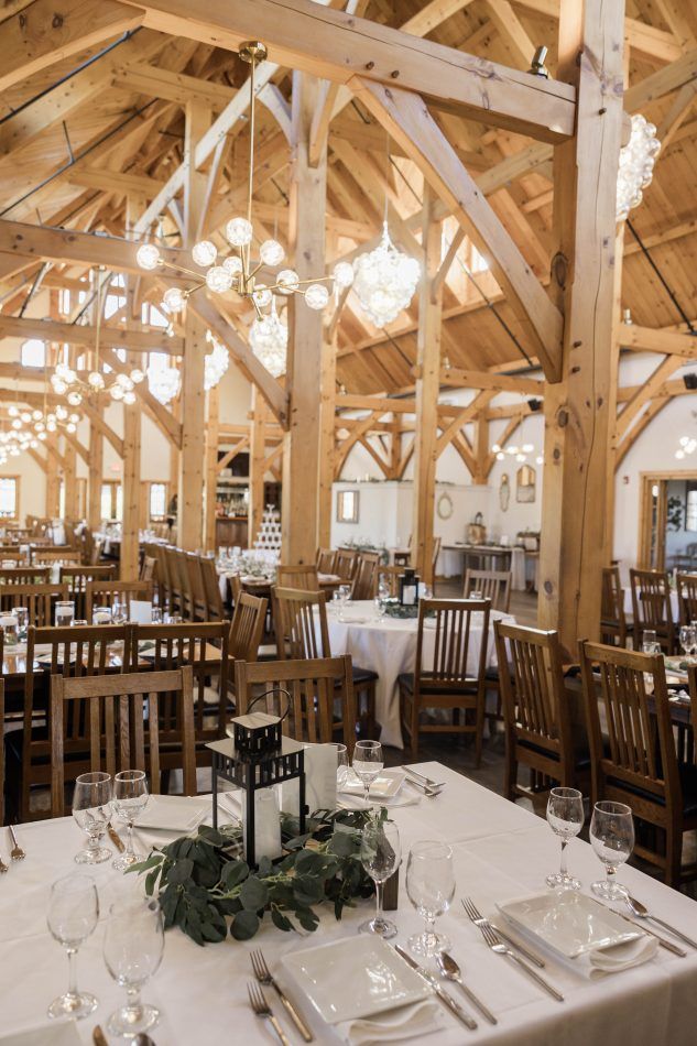 Elegant rustic barn wedding reception venue with exposed wooden beams and tables set with white linens and crystal glassware.