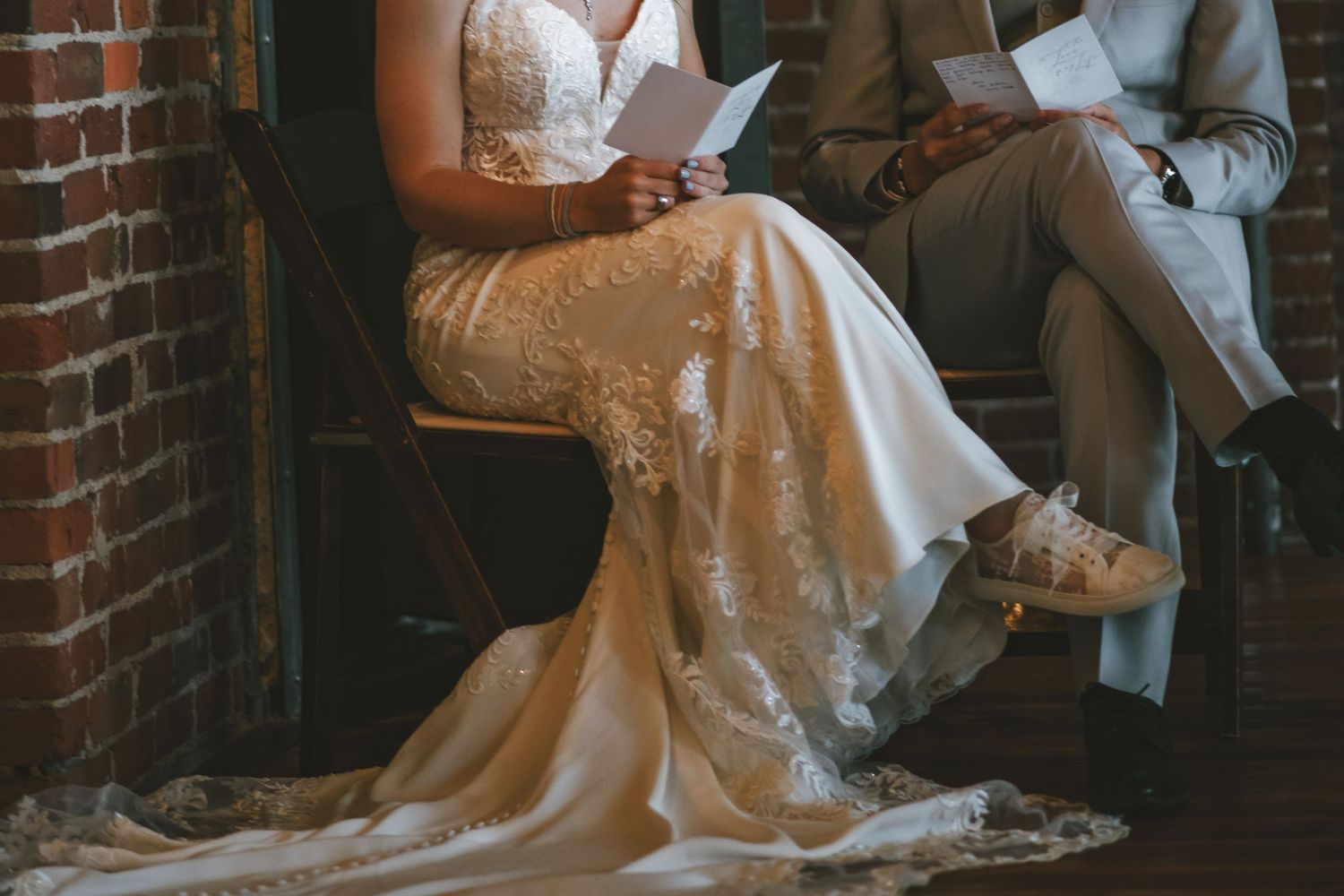 A bride in a flowing white gown sits elegantly on rustic brick steps while holding a bouquet of flowers.
