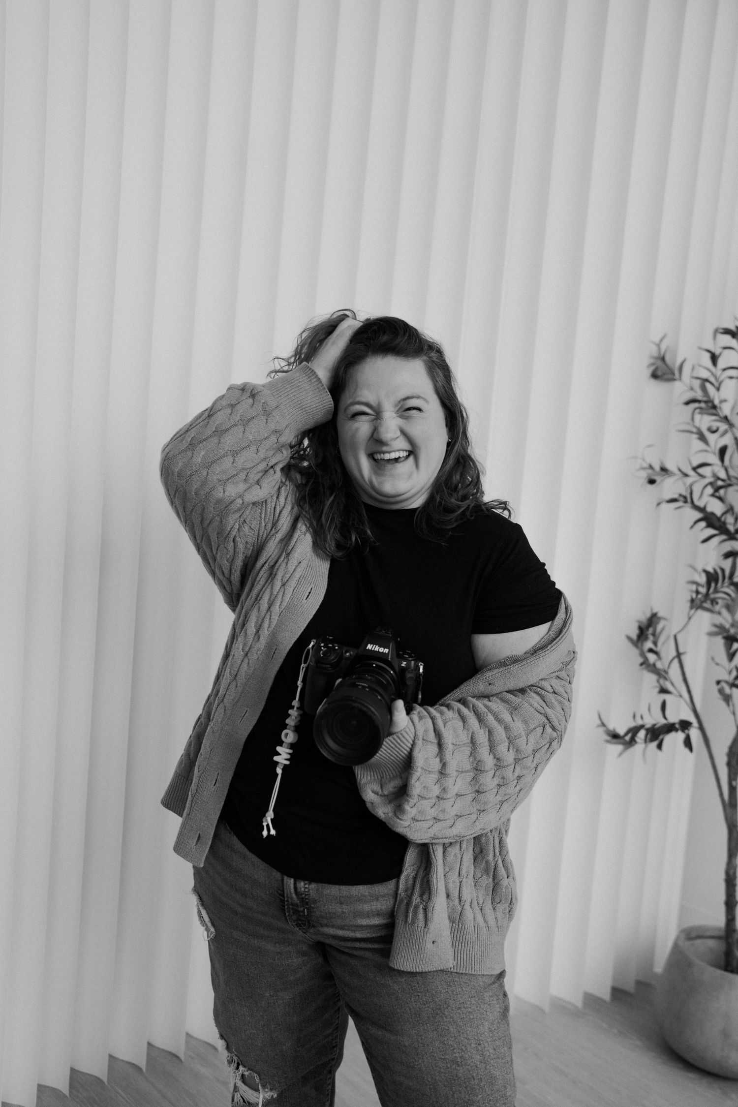 Black and white portrait of a laughing female photographer holding a camera in a bright studio.
