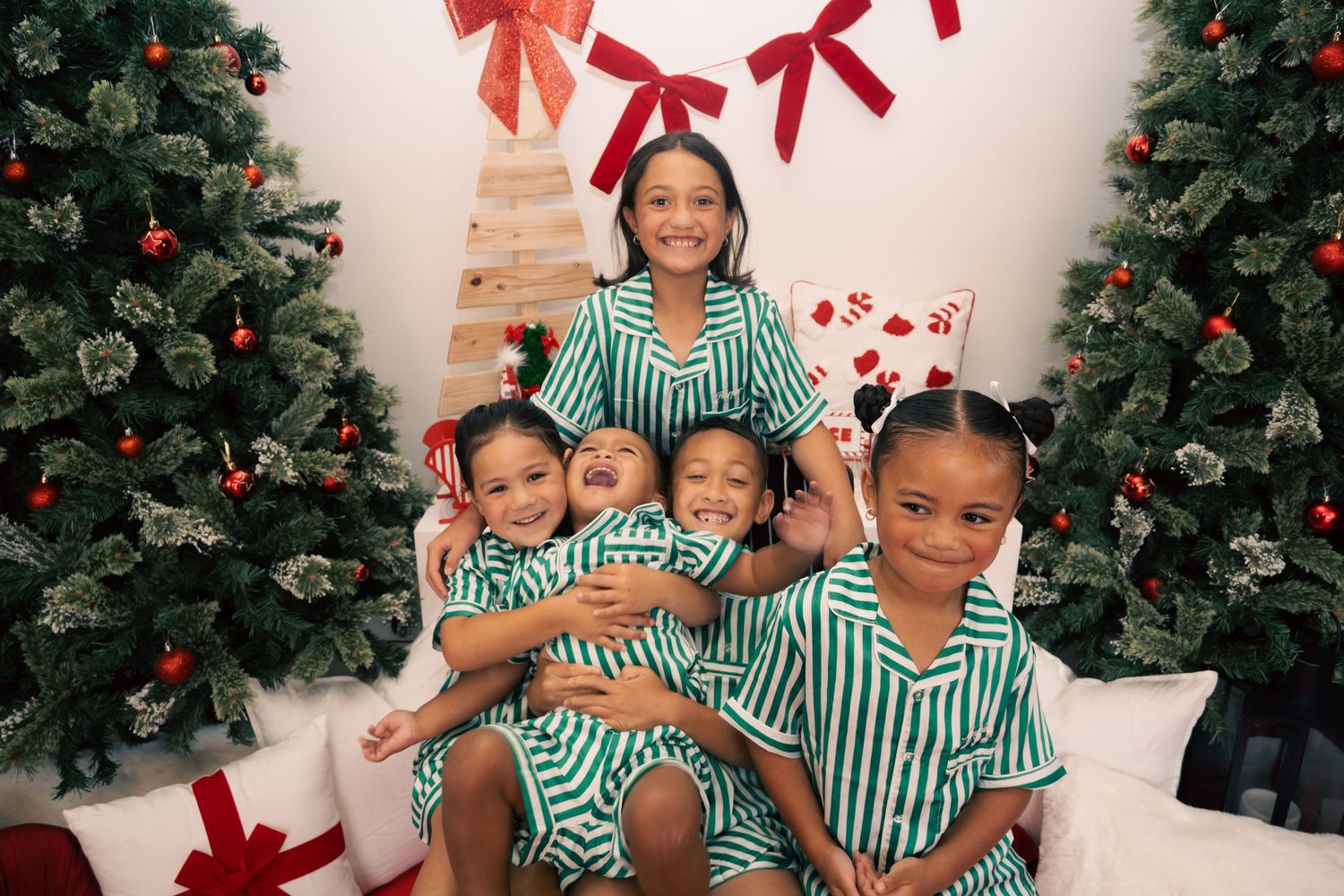 Family in matching green striped pajamas posing by Christmas trees with red bows and holiday decorations.