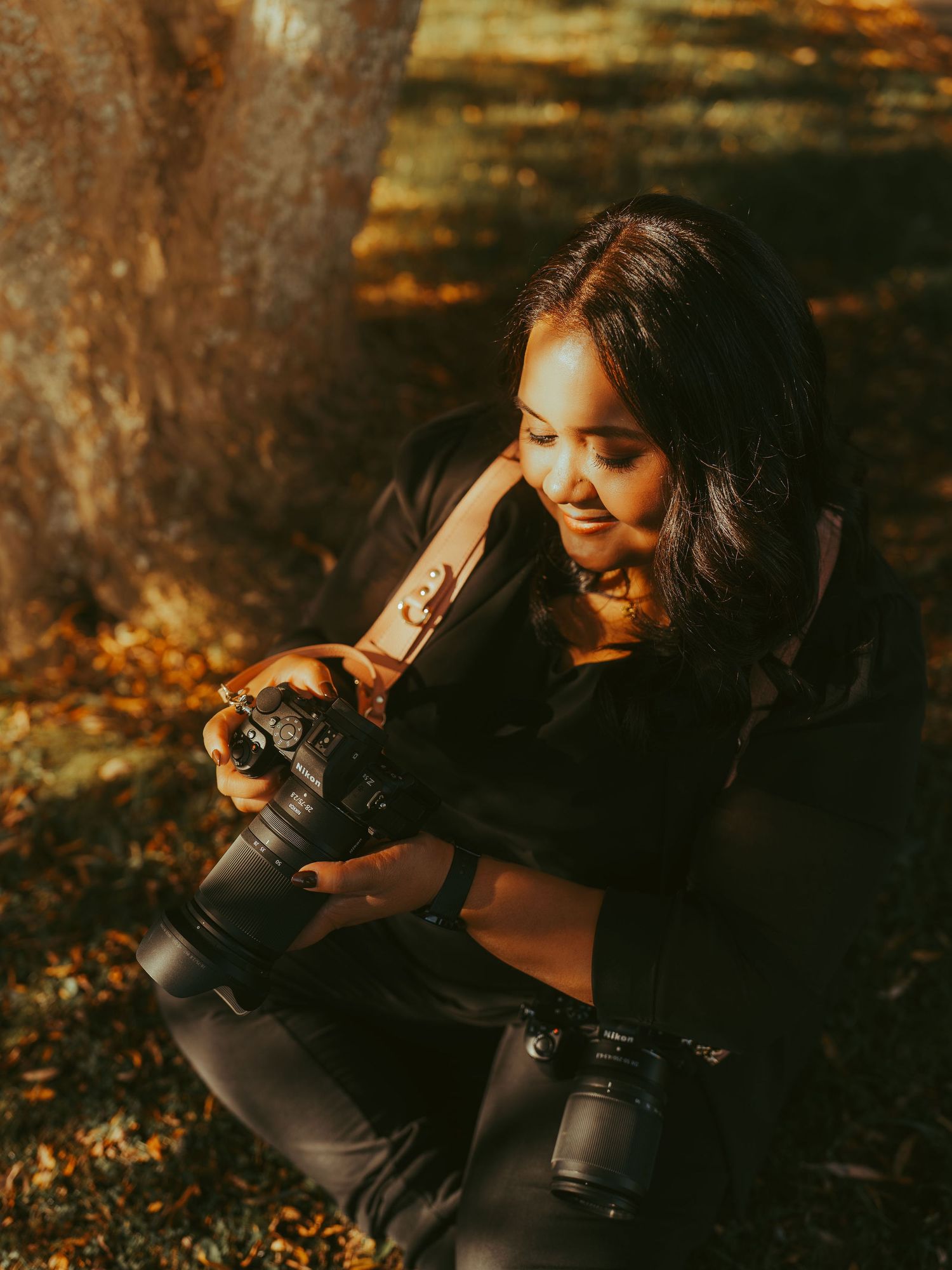 Woman smiling while reviewing photos on a DSLR camera outdoors in autumn setting.