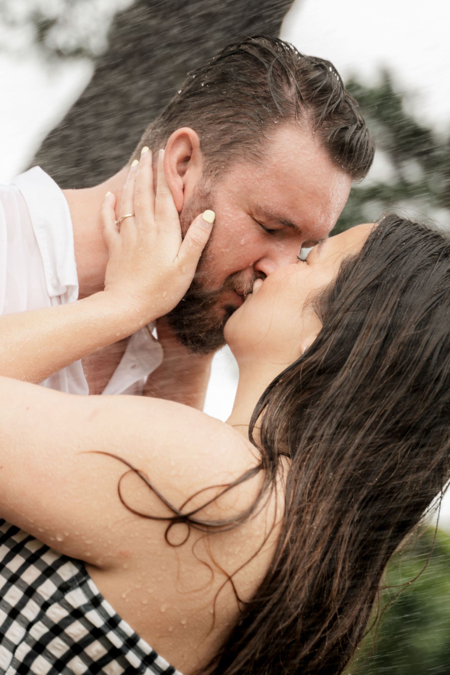 Couple sharing a passionate kiss in the rain, with wet hair and romantic embrace outdoors.