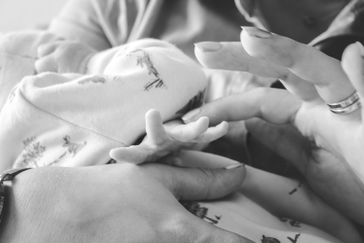 Black and white photo of a newborn baby's tiny hand being gently held by an adult's hands.