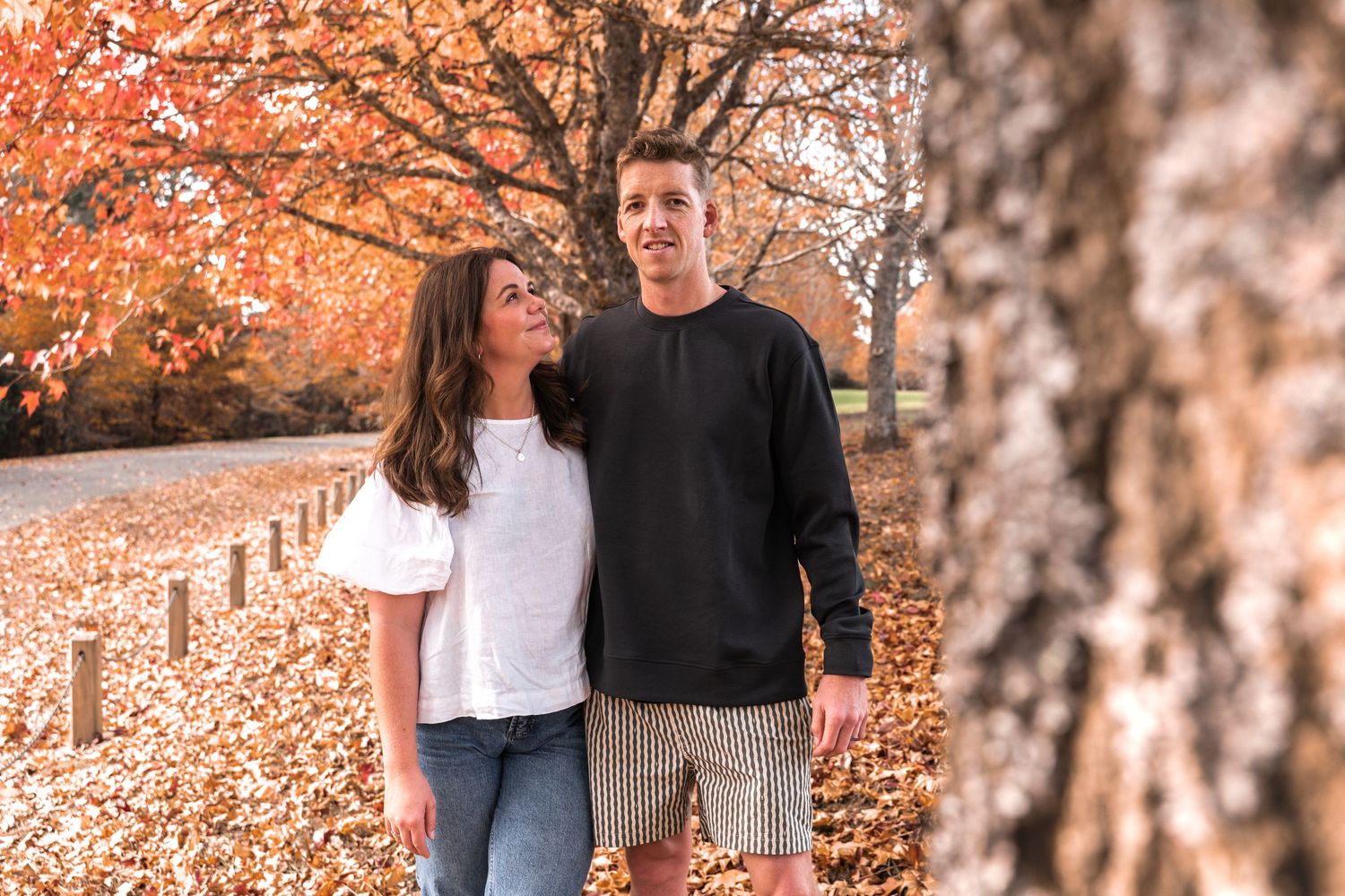 Couple smiling together outdoors in autumn park with colorful fall foliage and fallen leaves.
