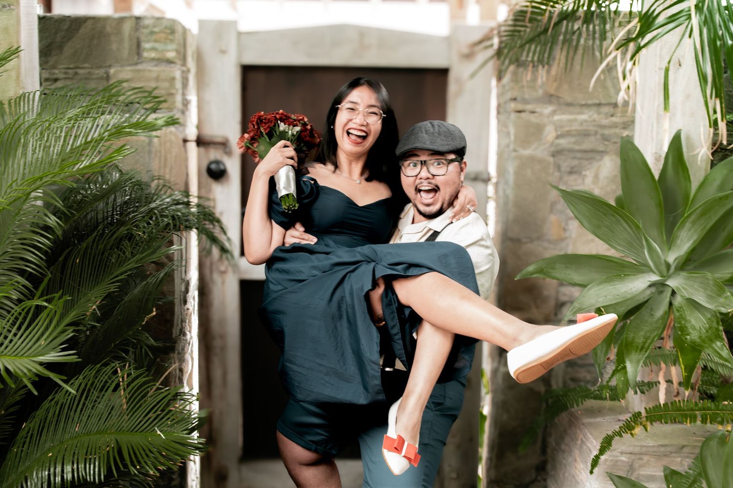 Joyful bride and groom celebrates their auckland wedding with champagne and flowers in a tropical courtyard setting.
