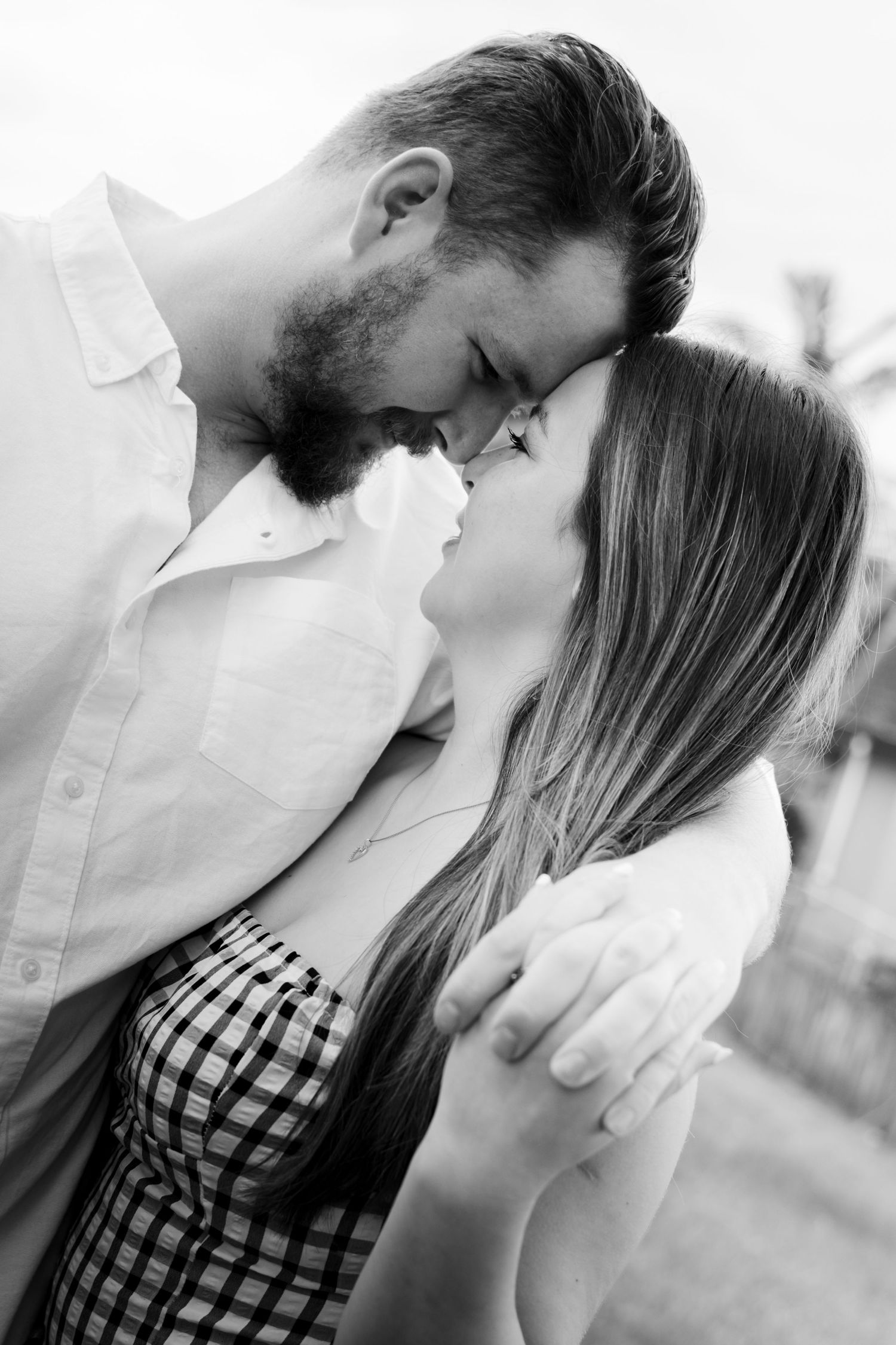 Black and white photo of a romantic couple sharing an intimate moment, touching foreheads and about to kiss outdoors.