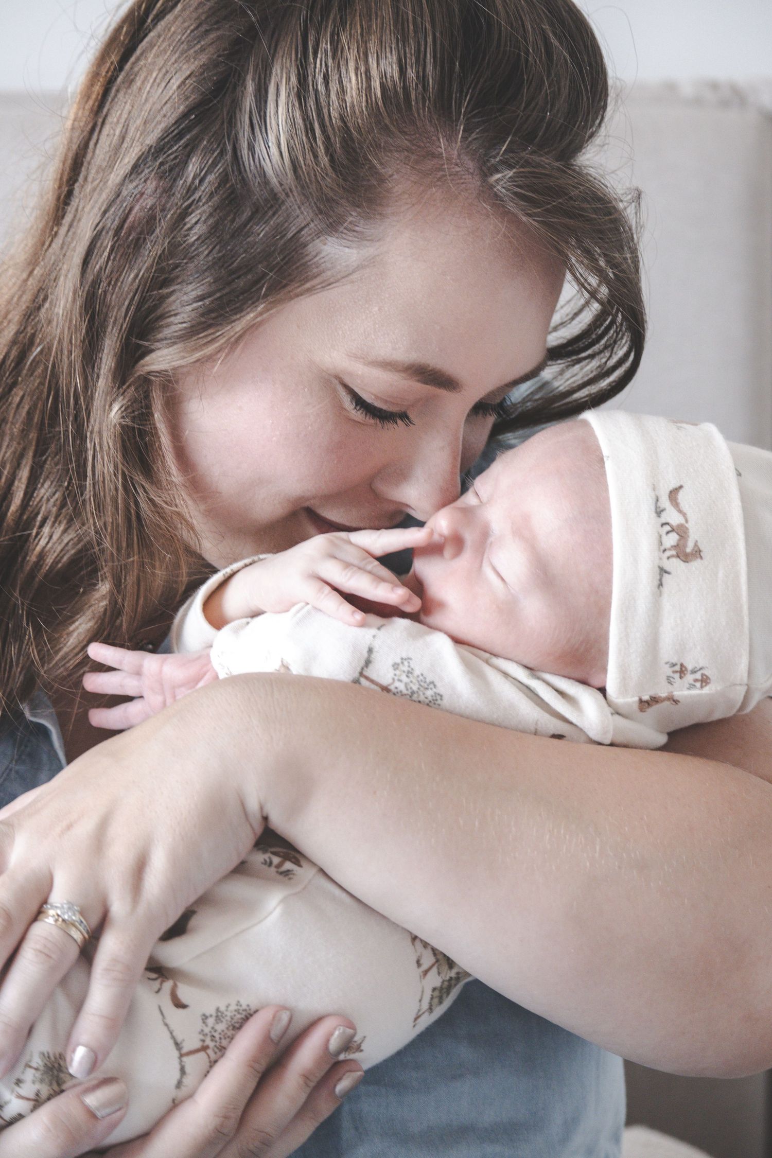 A young mother tenderly nuzzles her newborn baby wrapped in a floral onesie, sharing a loving moment.