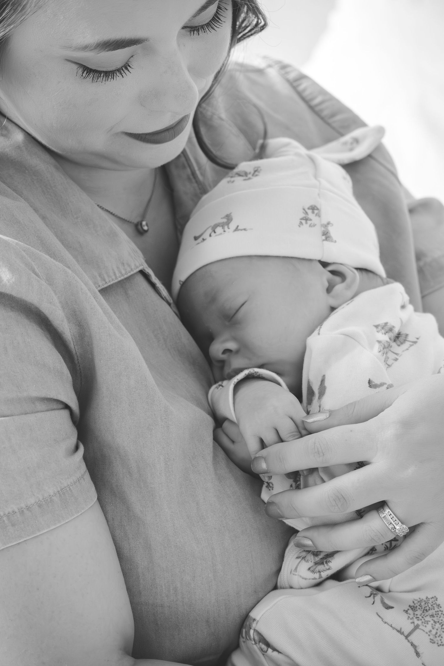 Black and white photo of a mother cradling her sleeping newborn baby wrapped in a swaddle blanket.