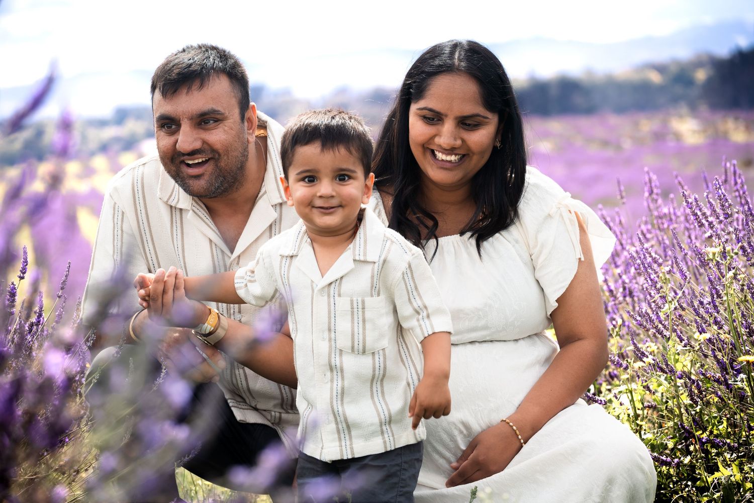Happy South Asian family with young boy posing in a vibrant purple lavender field, smiling together outdoors.