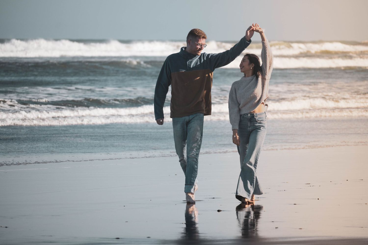 Couple dancing on a wet beach with ocean waves in the background on a cloudy day.