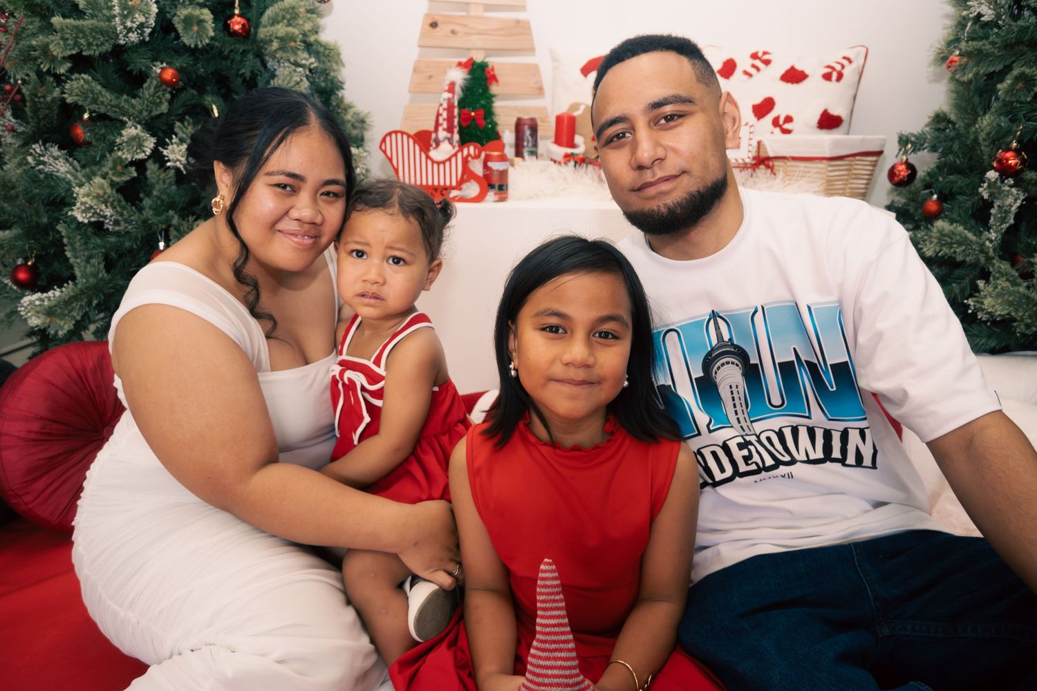 Family of four poses for a festive Christmas photo with holiday decorations and a Christmas tree in the background.