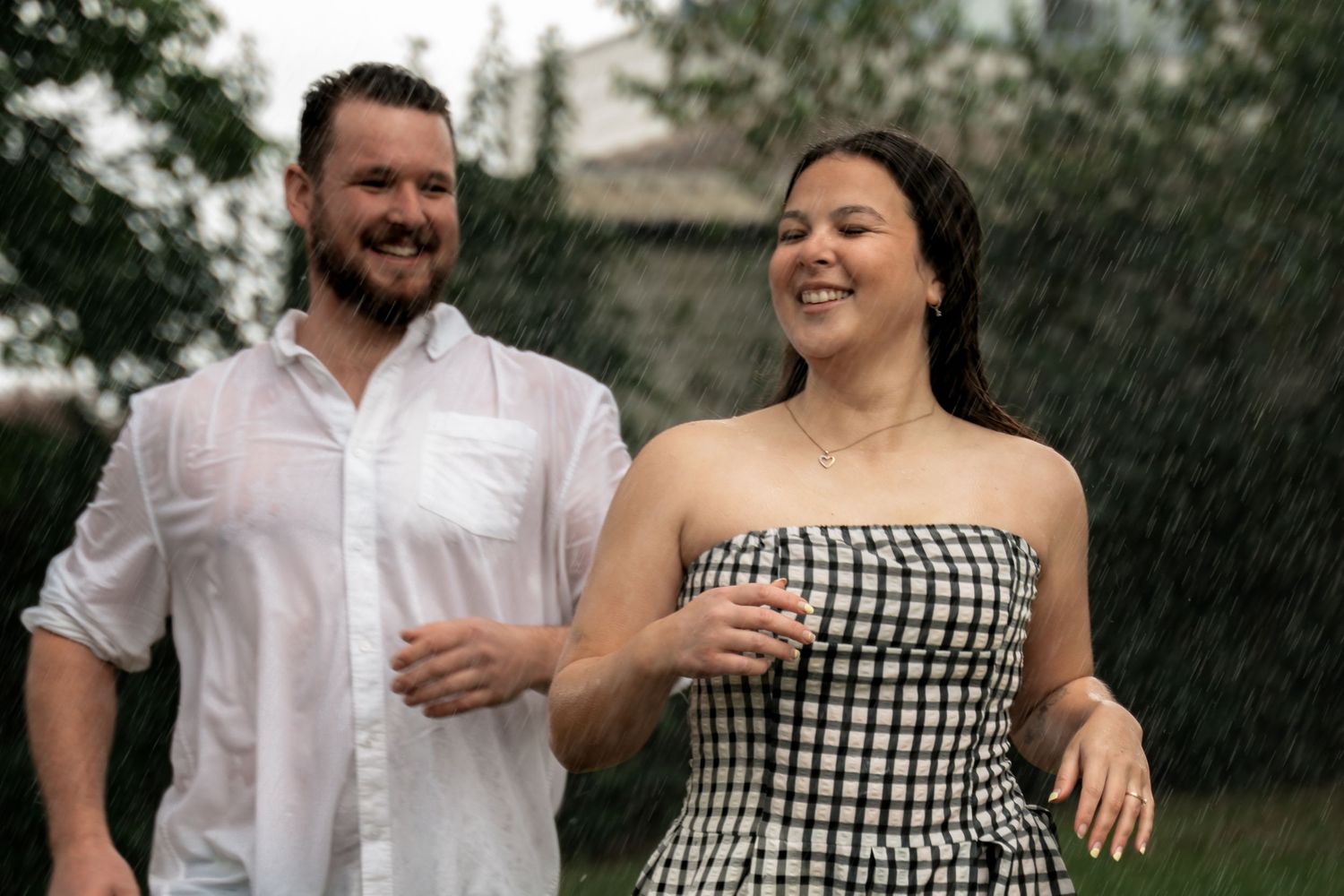 Happy couple laughing and dancing together in the rain, man in white shirt and woman in checkered dress.