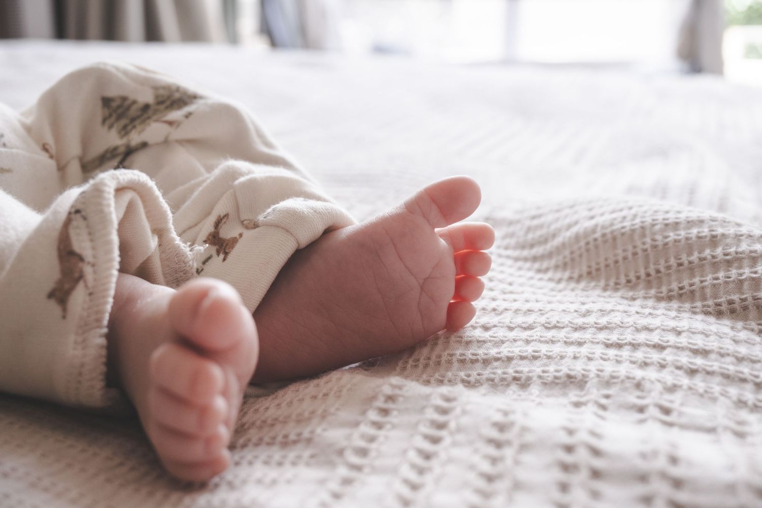 Close-up of newborn baby feet resting on a soft white knit blanket in cozy white patterned pajamas.