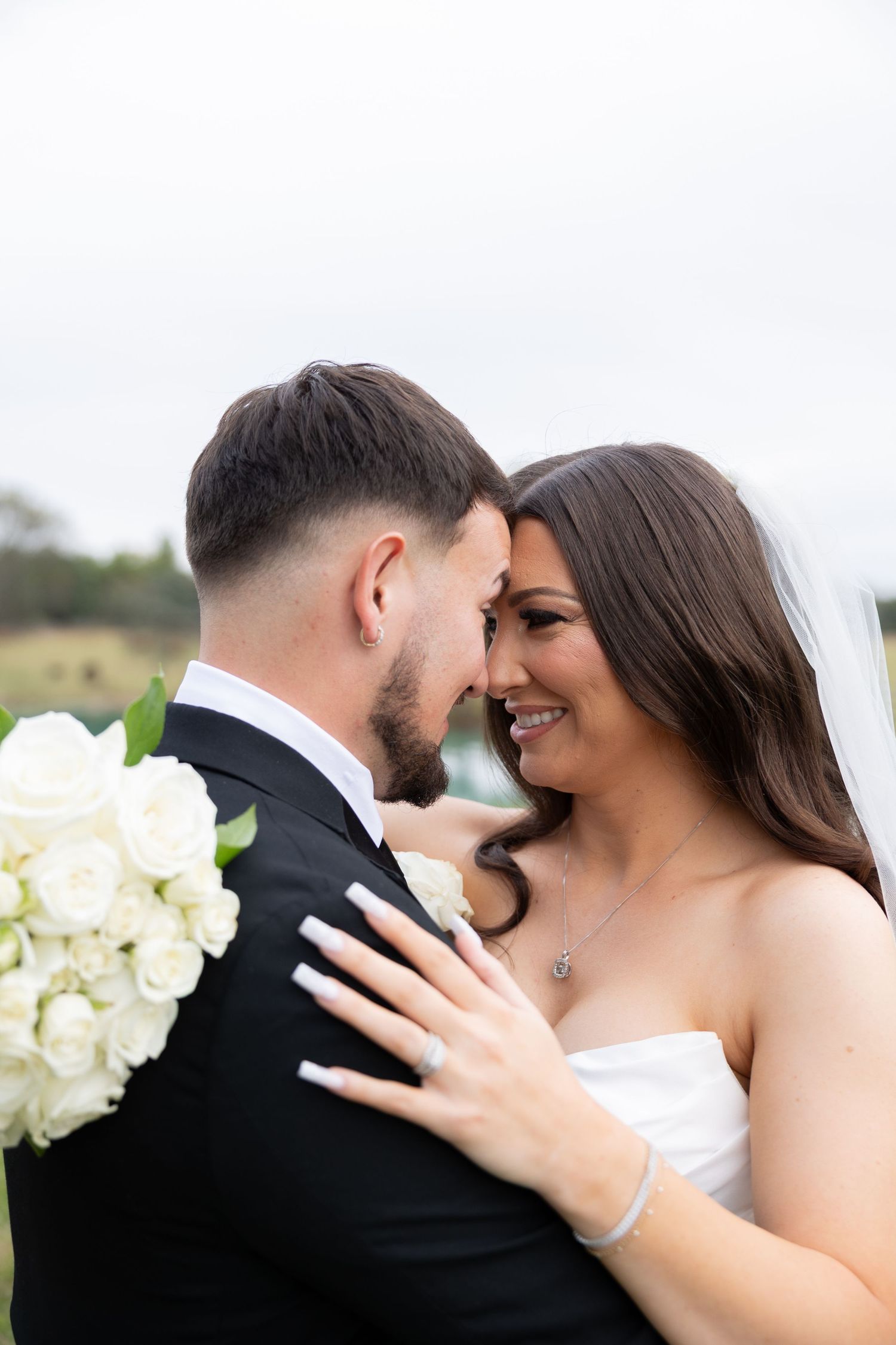 A bride and groom share an intimate moment, touching foreheads, as she holds his shoulder with a diamond ring visible.