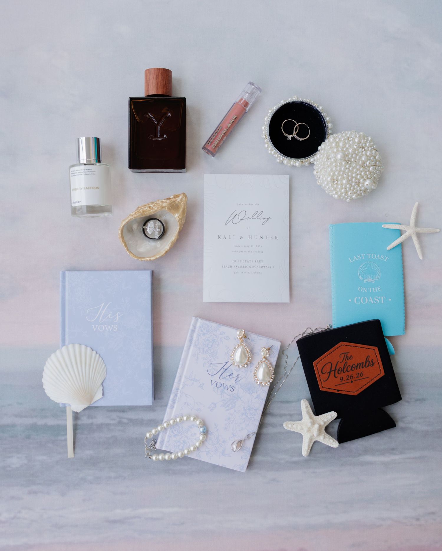 Elegant wedding flat lay with perfume, rings, pearl earrings, starfish, invitations, and coastal accessories on marble.