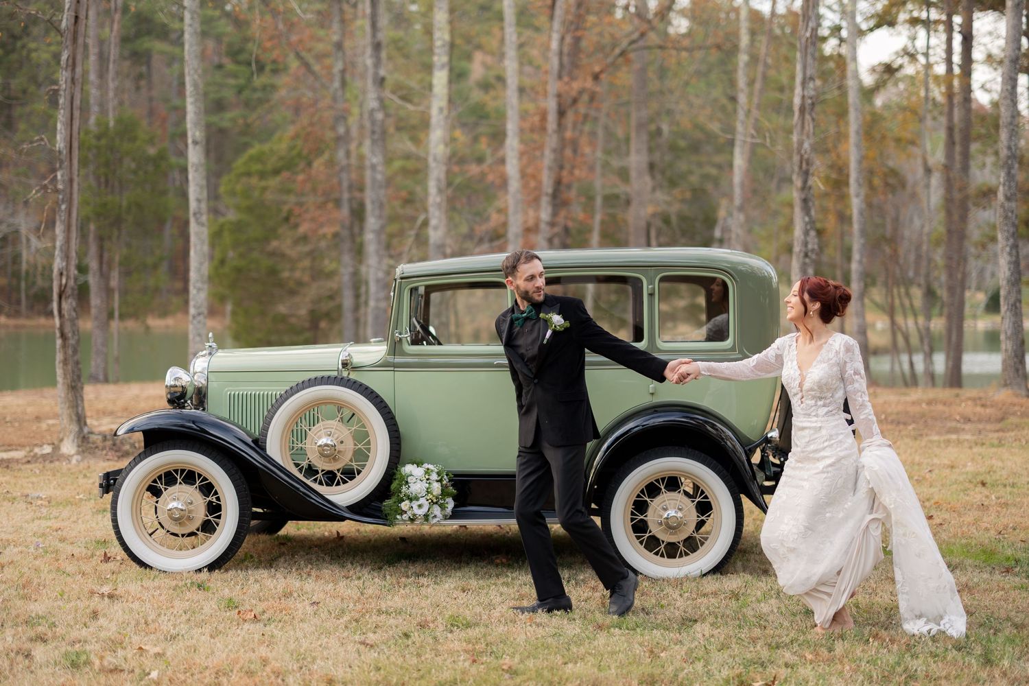 Bride and groom posing with a vintage green antique car outdoors at a rustic woodland wedding venue.