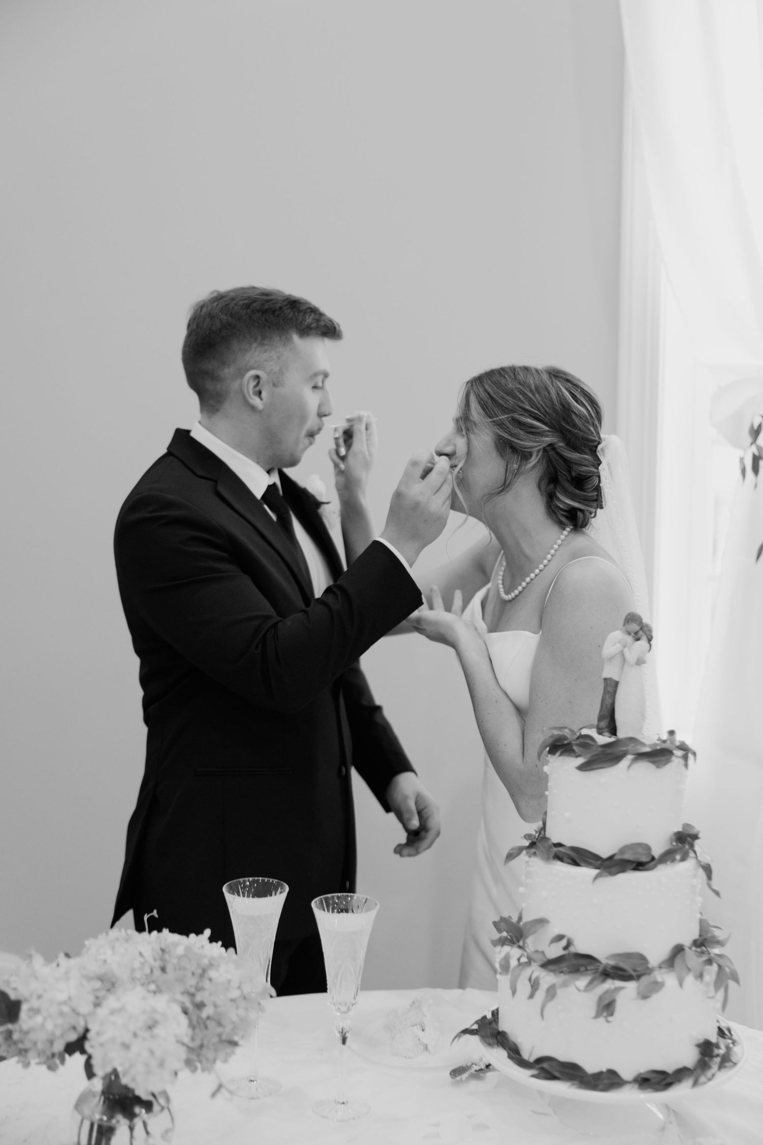 Black and white photo of bride and groom feeding each other wedding cake at their reception.