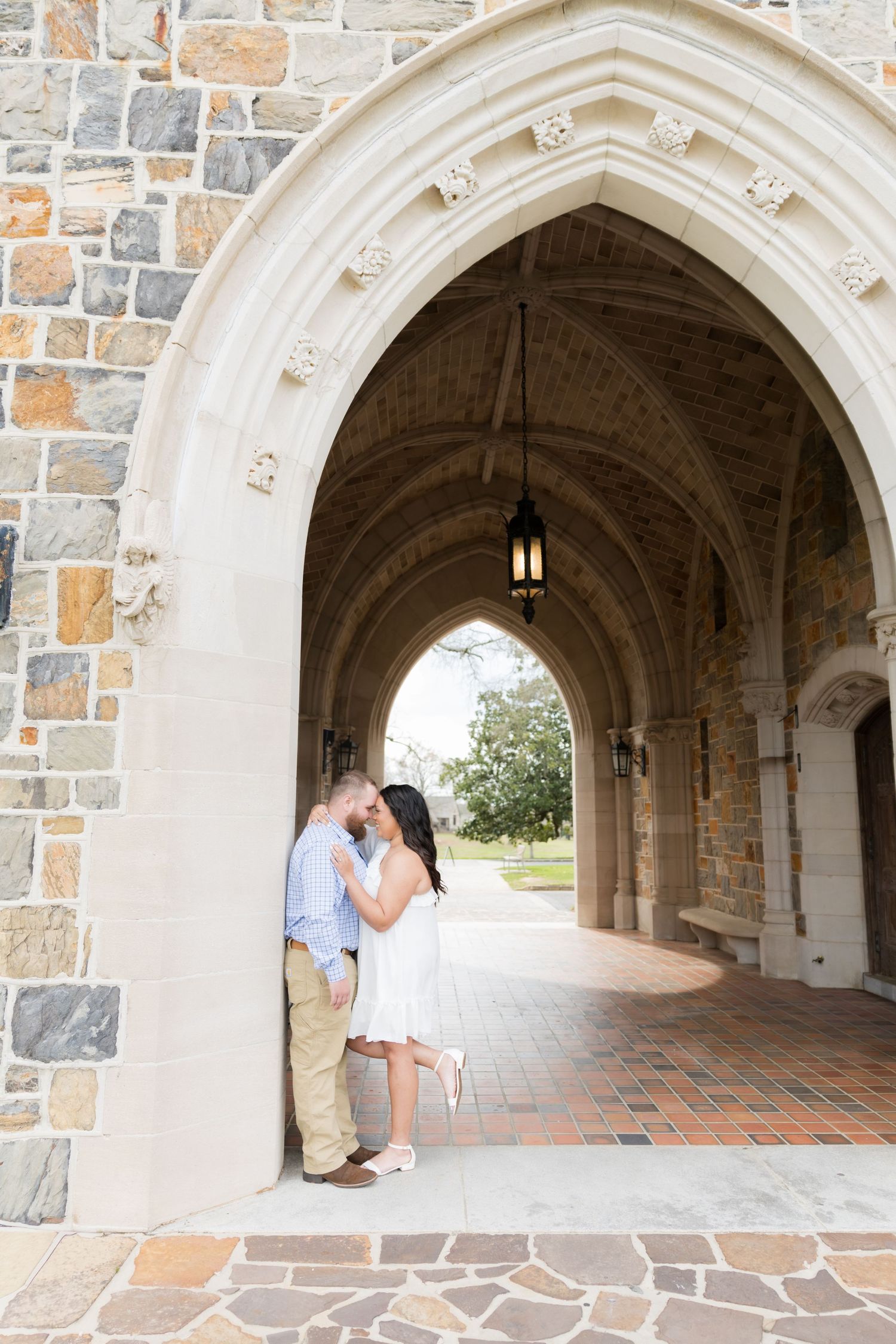 Couple sharing a romantic moment under a Gothic stone archway at a historic university building.