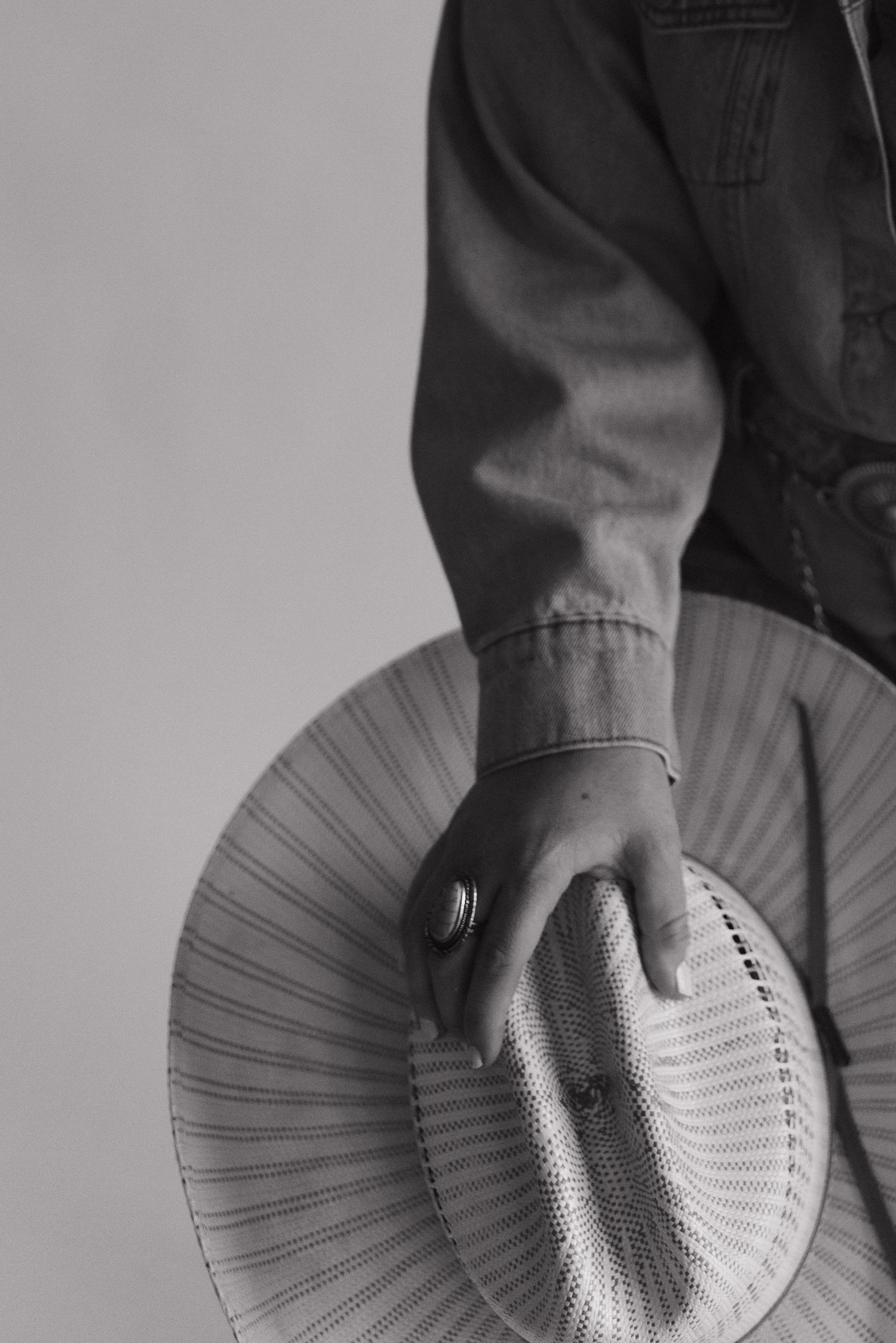 Black and white photo of person holding a straw hat at their side.