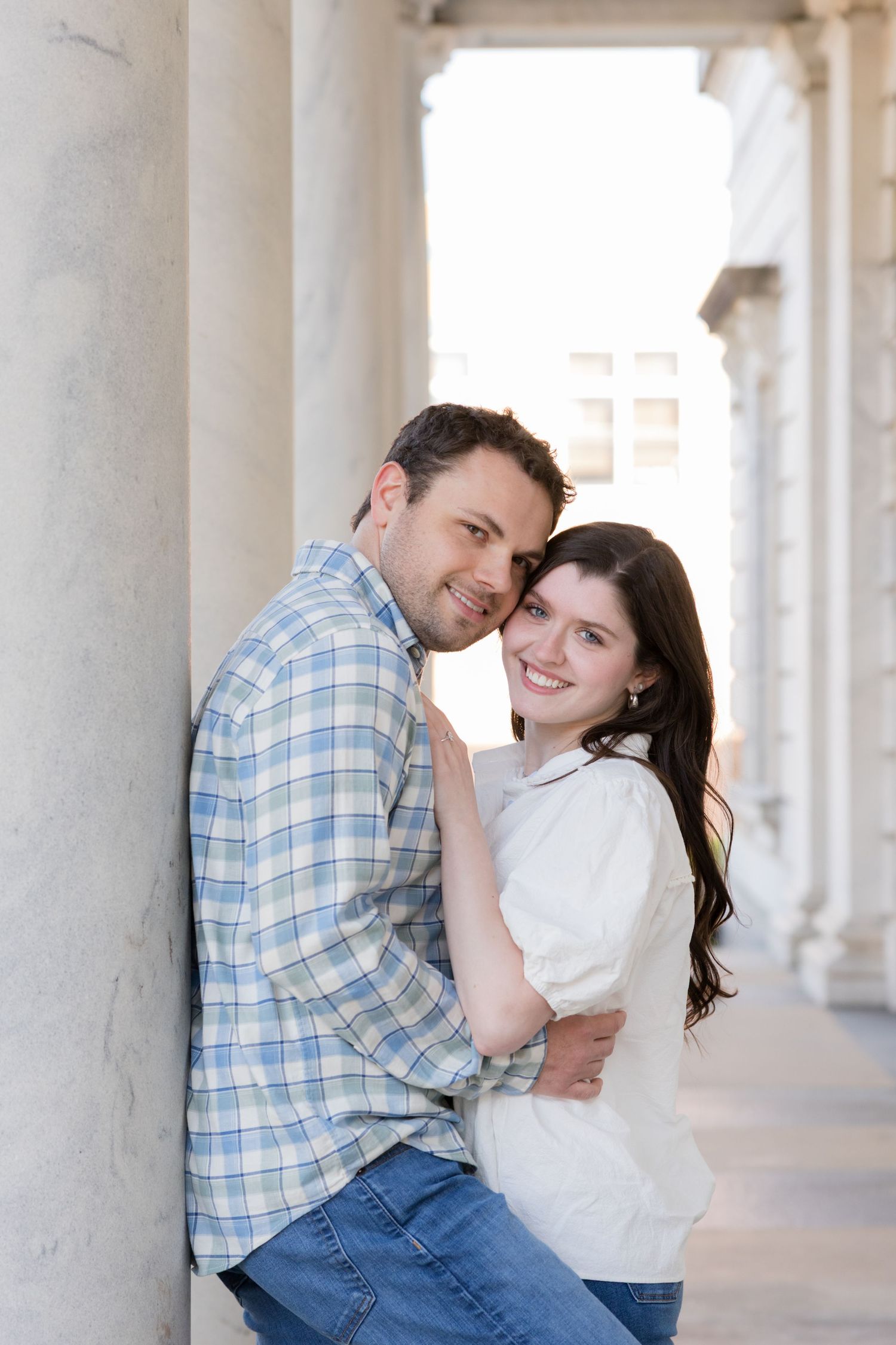 Happy couple embracing and smiling by marble columns, man in plaid shirt and woman in white top.