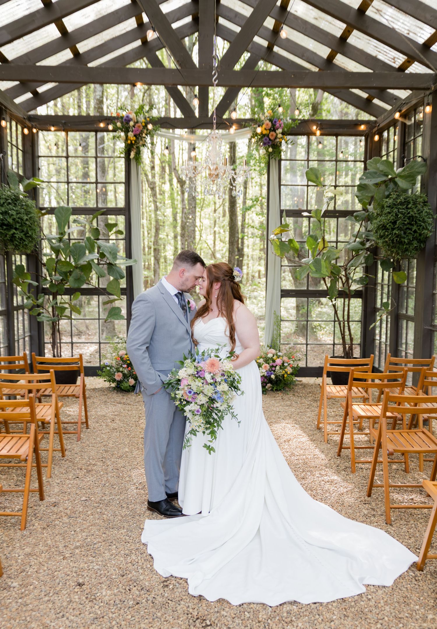 Bride and groom share a romantic moment at a glass greenhouse wedding ceremony venue surrounded by lush greenery and floral arrangements.