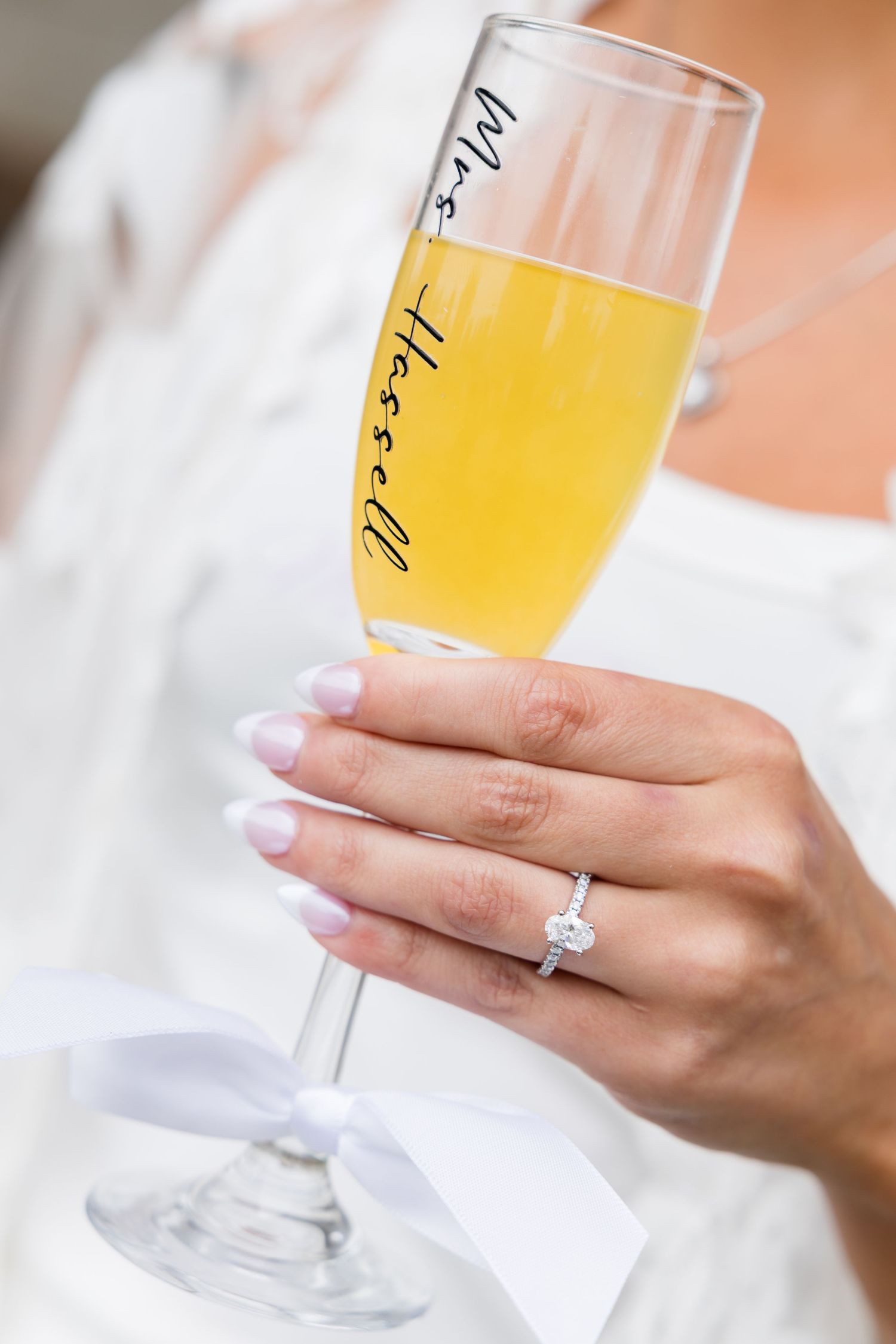 Bride holding a personalized Mrs. Hessell champagne flute with a diamond engagement ring on her finger.