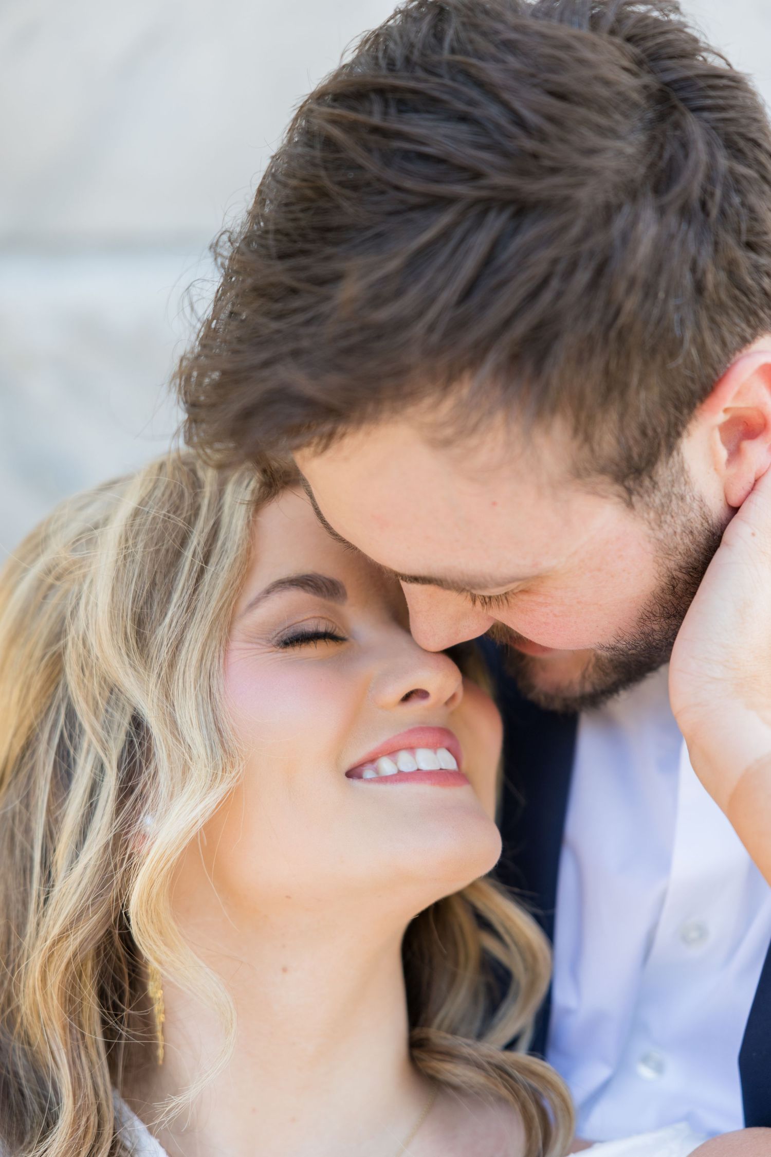 A smiling blonde woman and bearded man share a romantic forehead-to-forehead moment in a tender couples portrait.