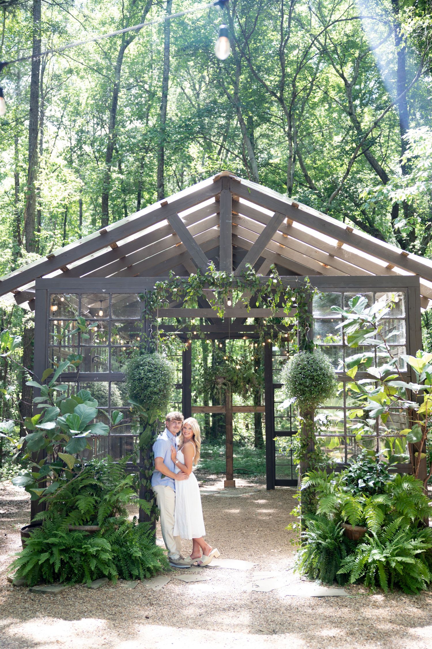 Couple embracing in a lush garden greenhouse wedding venue surrounded by ferns and topiaries in a forest setting.