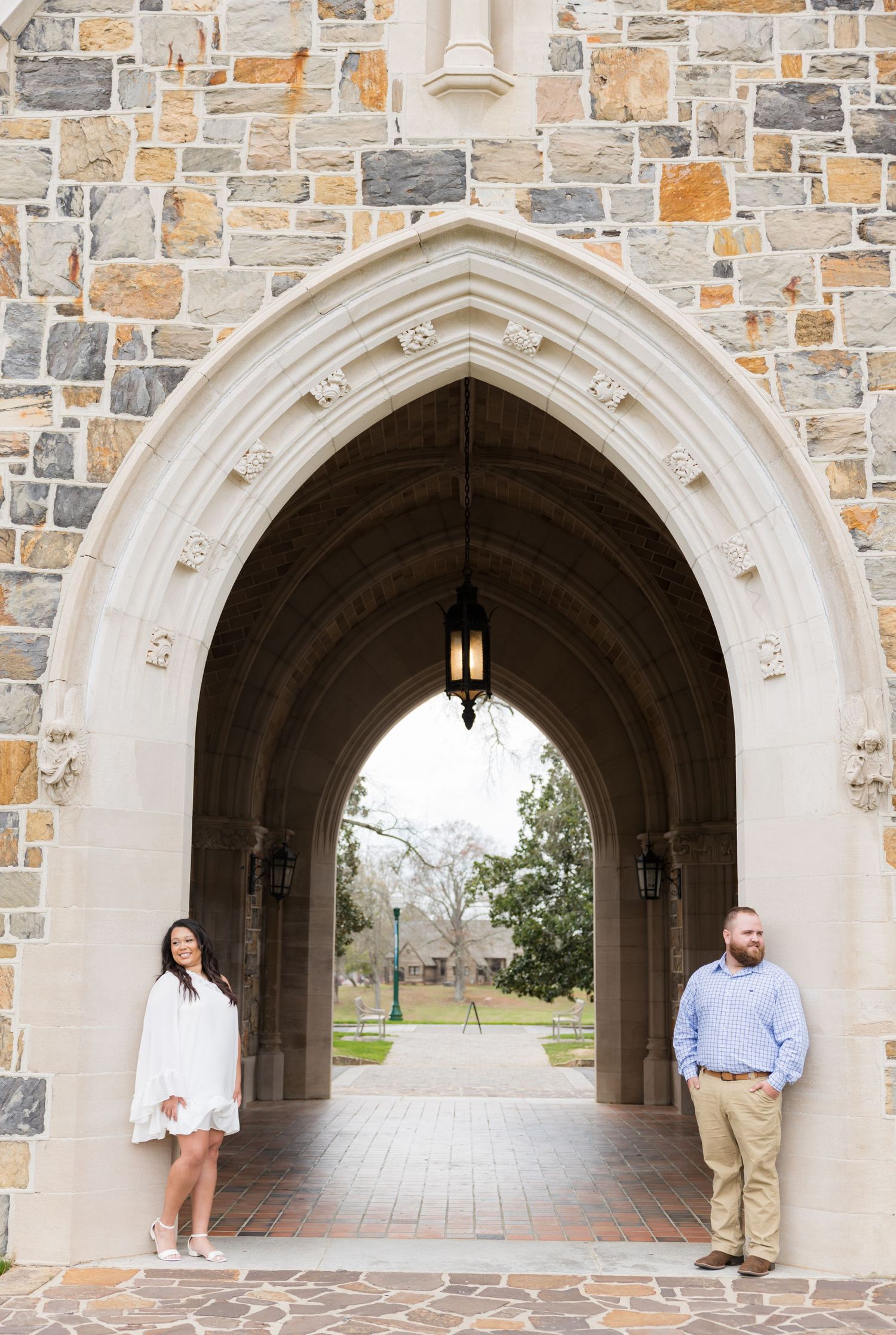 Couple posing under a Gothic stone archway with ornate details at a historic university campus.