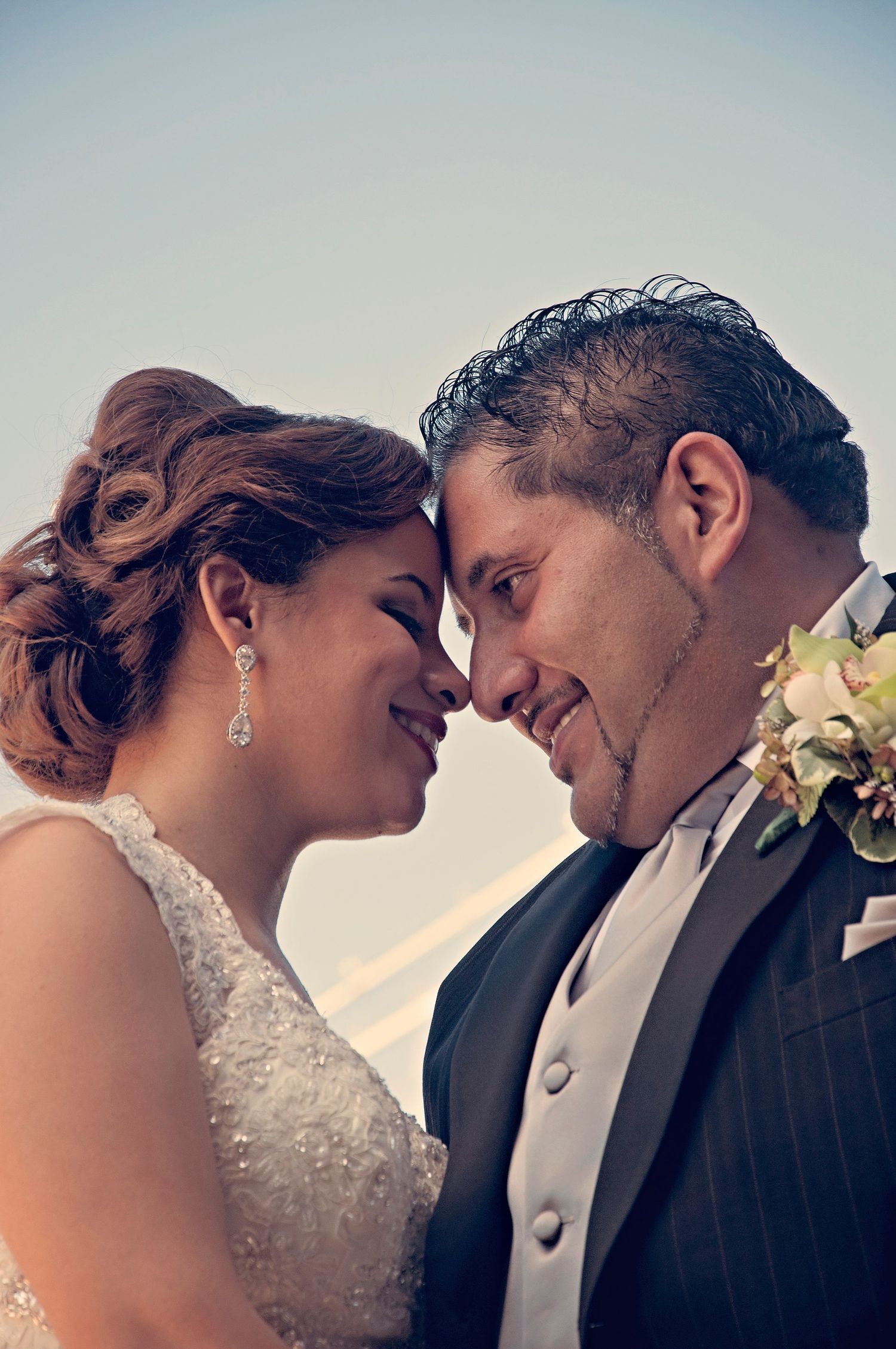 Bride and groom touch foreheads and smile tenderly in a romantic outdoor wedding portrait.