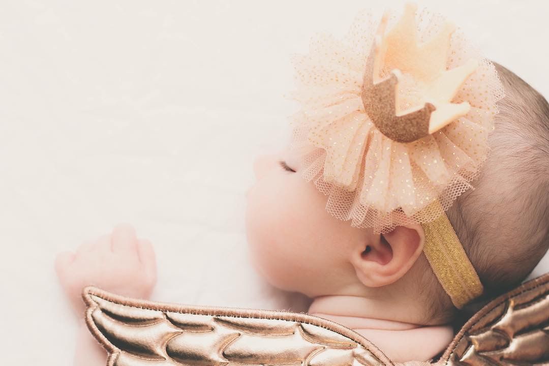 Sleeping baby wearing a golden crown headband with tulle and angel wings costume.
