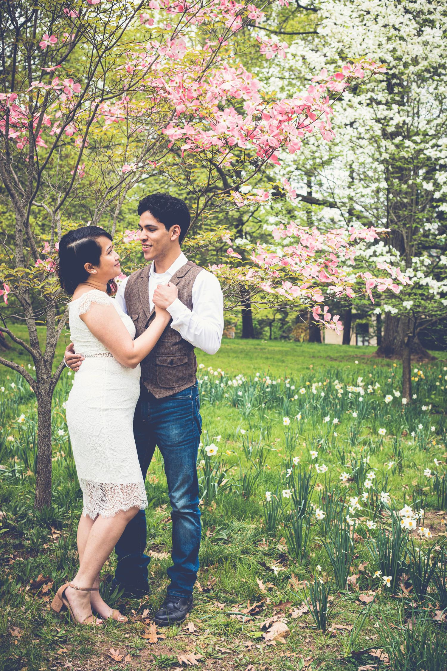 Engaged couple dancing together under blooming pink and white dogwood trees in a lush green park.