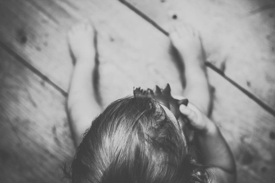 Black and white photo of a young child lying on a wooden floor, viewed from above.