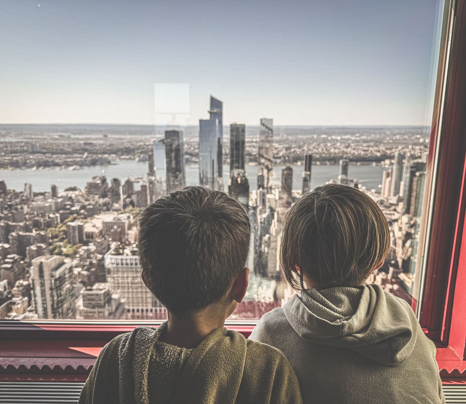 Two children gaze at a stunning city skyline from a high-rise observation deck overlooking a vast urban landscape.
