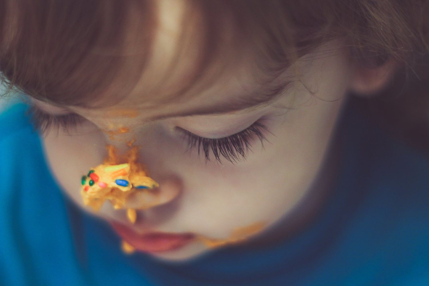 Close-up of a young child with a small orange toy dinosaur balanced on their nose.